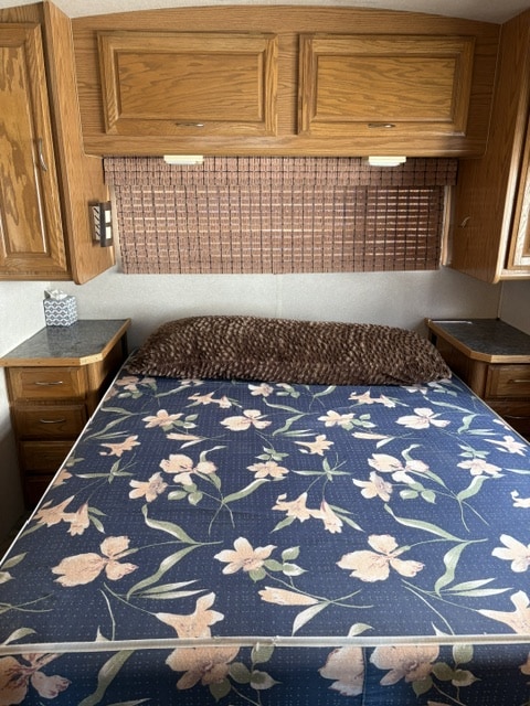 RV rental bedroom featuring a floral bedspread, wooden overhead cabinets, and bedside tables, providing a cozy sleeping area.. Fleetwood Bounder 1994