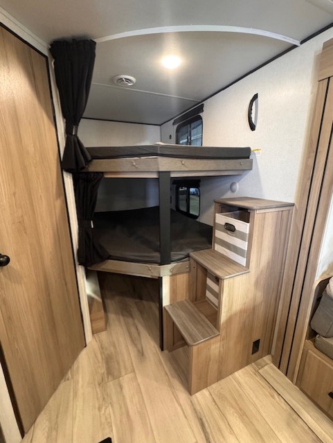 This RV rental shows a modern sleeping area with two bunk beds, privacy curtains, and built-in steps for easy access.. Keystone RV Coleman Lantern 2025