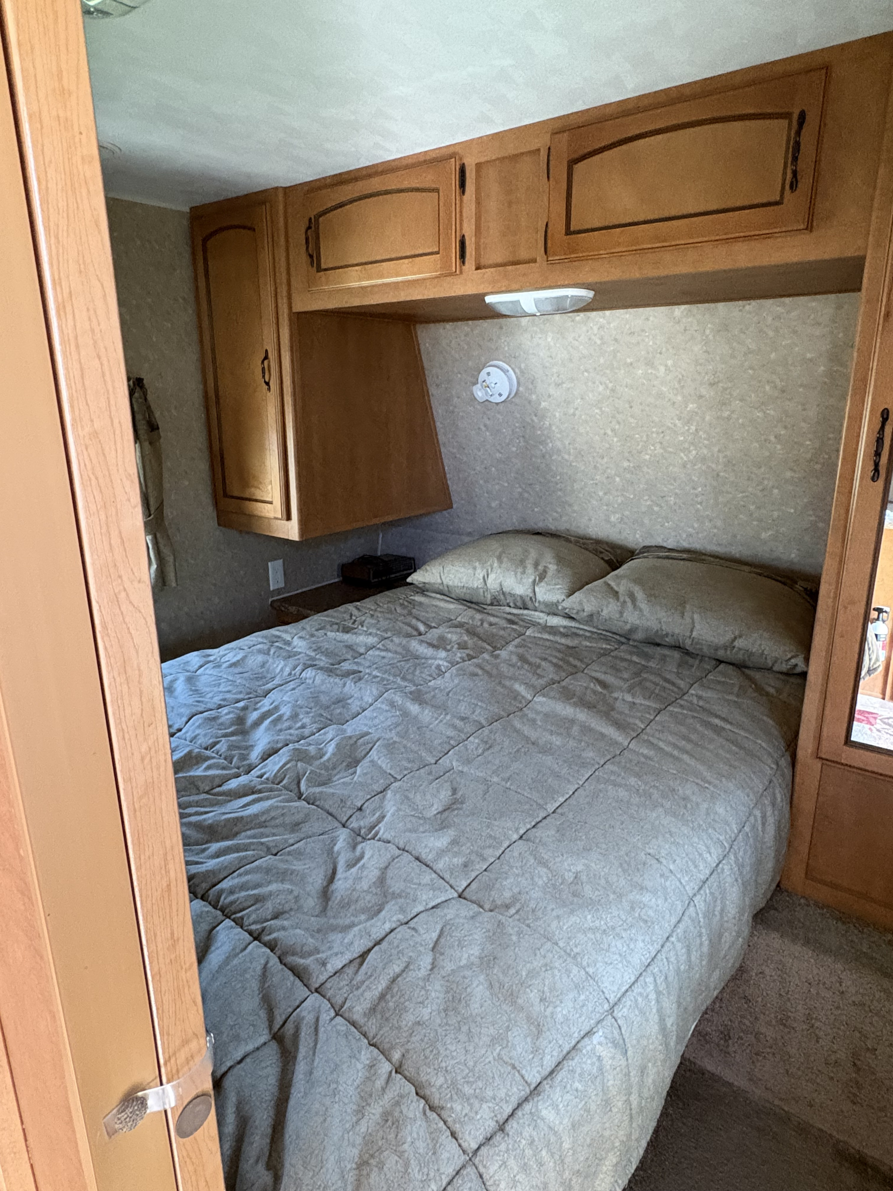 Inviting RV rental bedroom with a bed, grey quilted comforter, and warm wooden cabinets. Ideal for compact stays.. Forest River Palomino Puma 2011