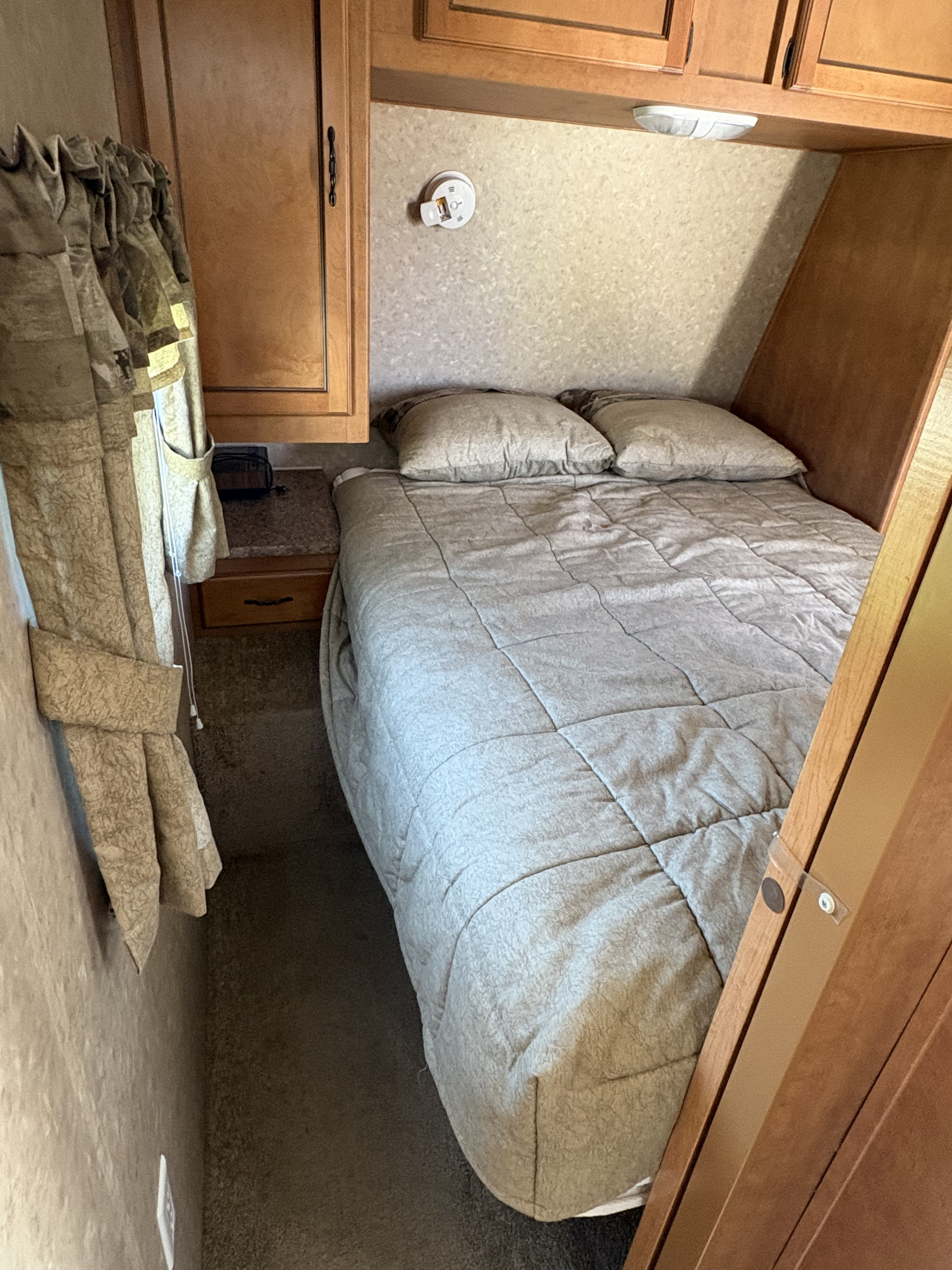 This RV rental features a compact bedroom with a cozy bed, ample storage via overhead cabinets, and a small nightstand.. Forest River Palomino Puma 2011