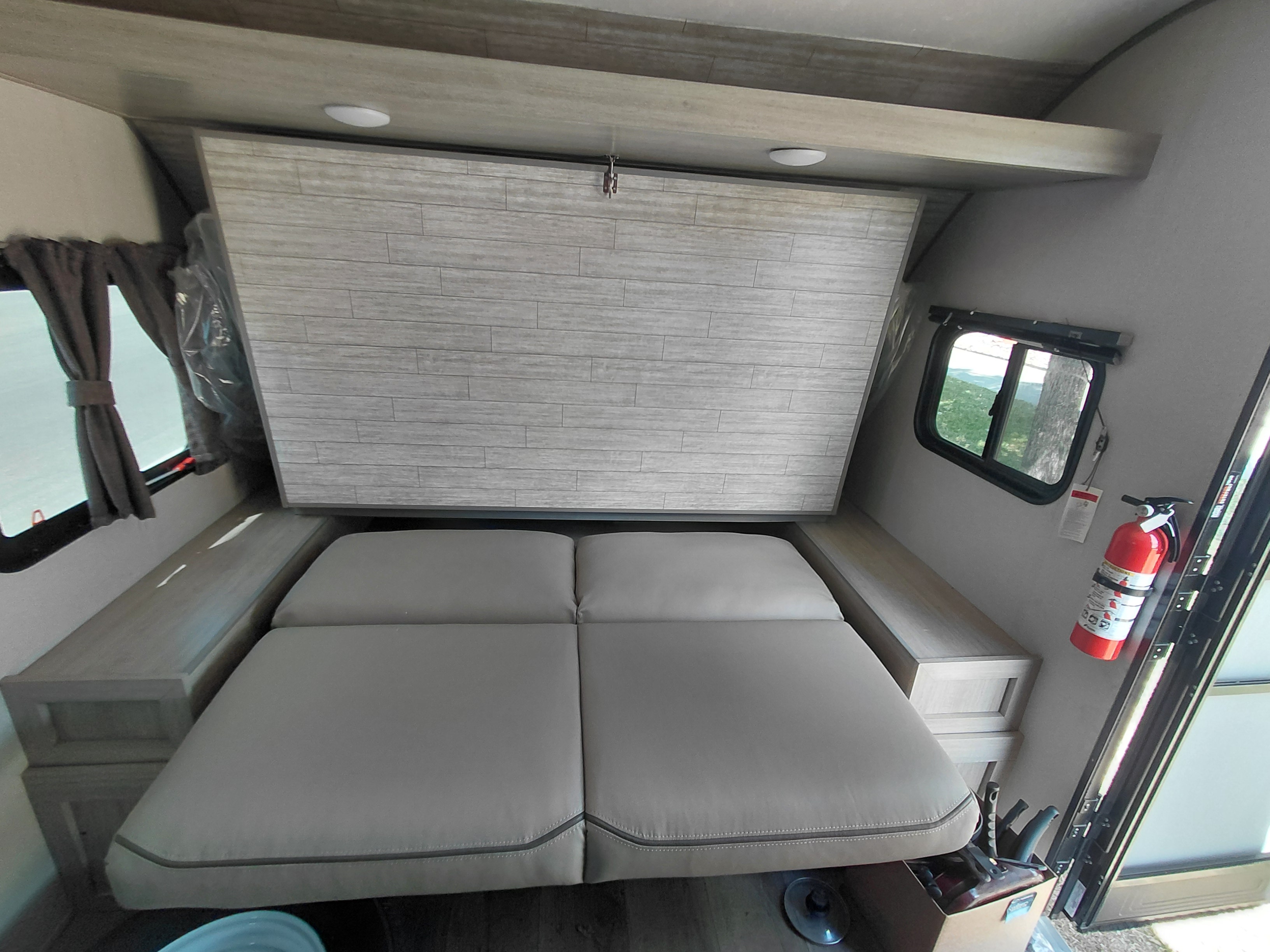Clean RV rental interior: a versatile bed with built-in storage, side windows, and a safety fire extinguisher. Ready for travel!. Coachmen Catalina Summit Series 2024