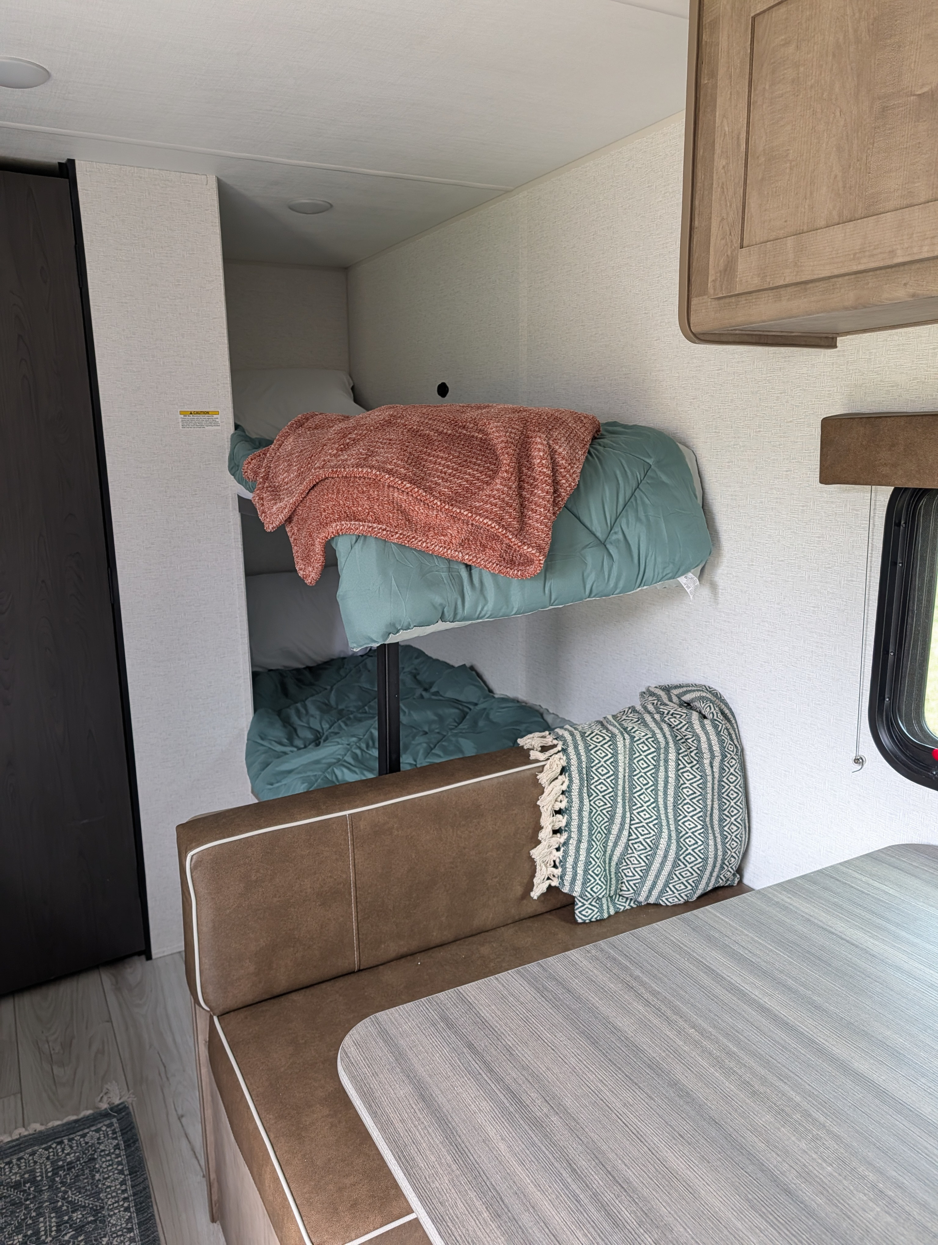 RV rental interior featuring bunk beds with teal and orange bedding, a brown dinette bench, and a light gray table.. Keystone RV Springdale Mini 2025