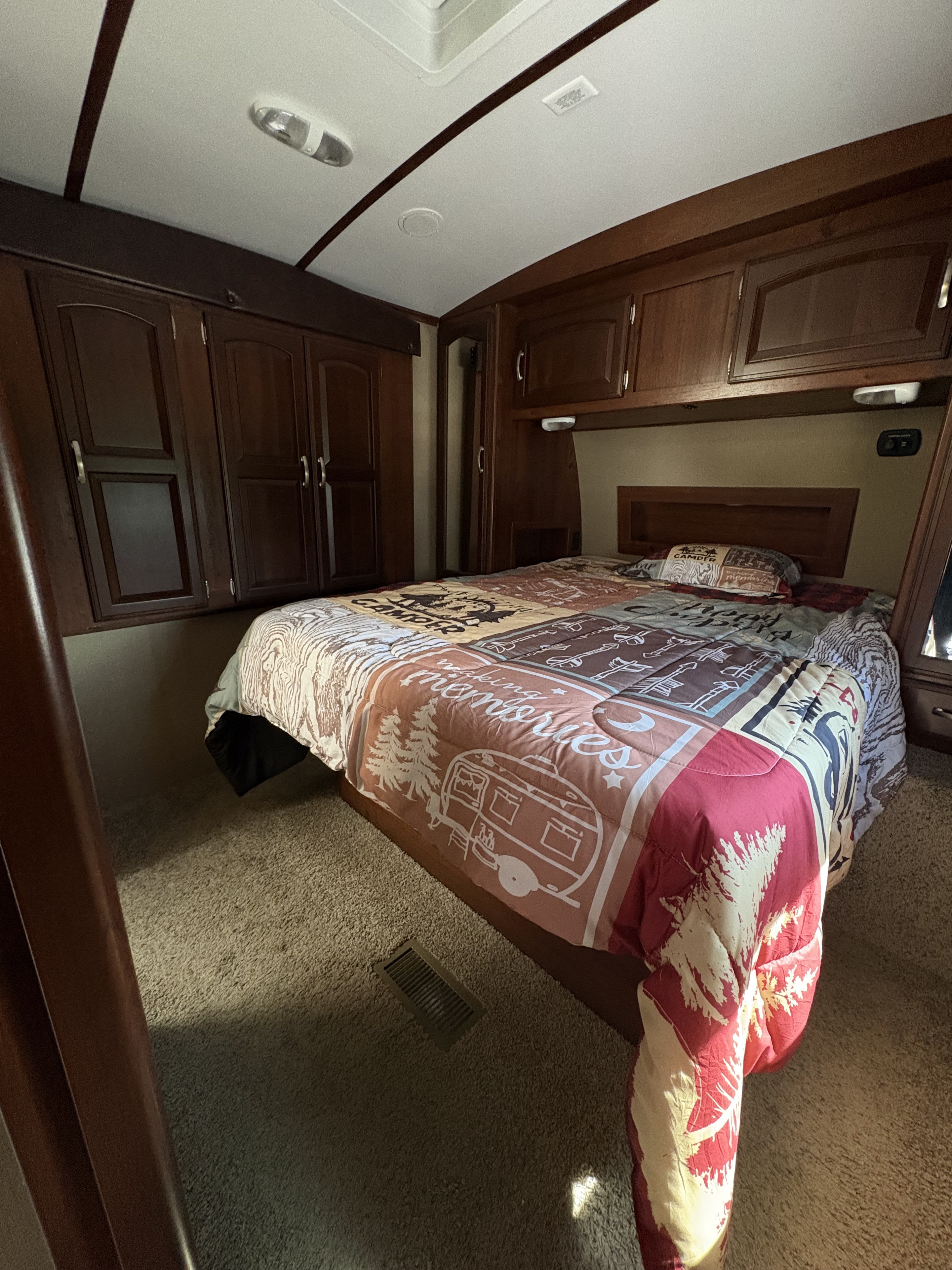Experience comfort in this RV rental bedroom: bed with 'making memories' comforter, wood cabinets, and carpet.. Keystone RV Outback Super-Lite 2015