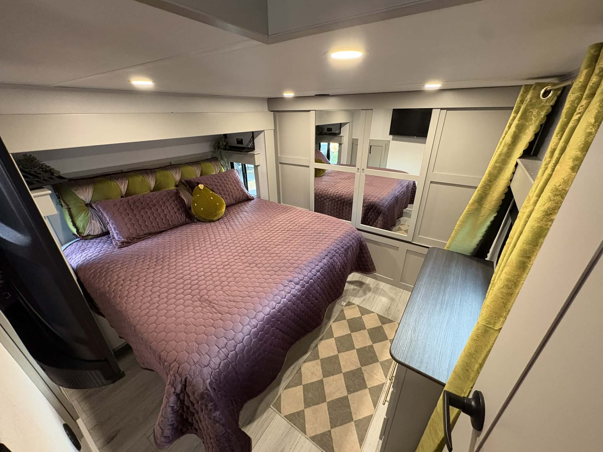 Cozy RV rental bedroom featuring a purple quilted bed, green tufted headboard, and mirrored closet, perfect for travel.. Keystone Montana High Country 2026