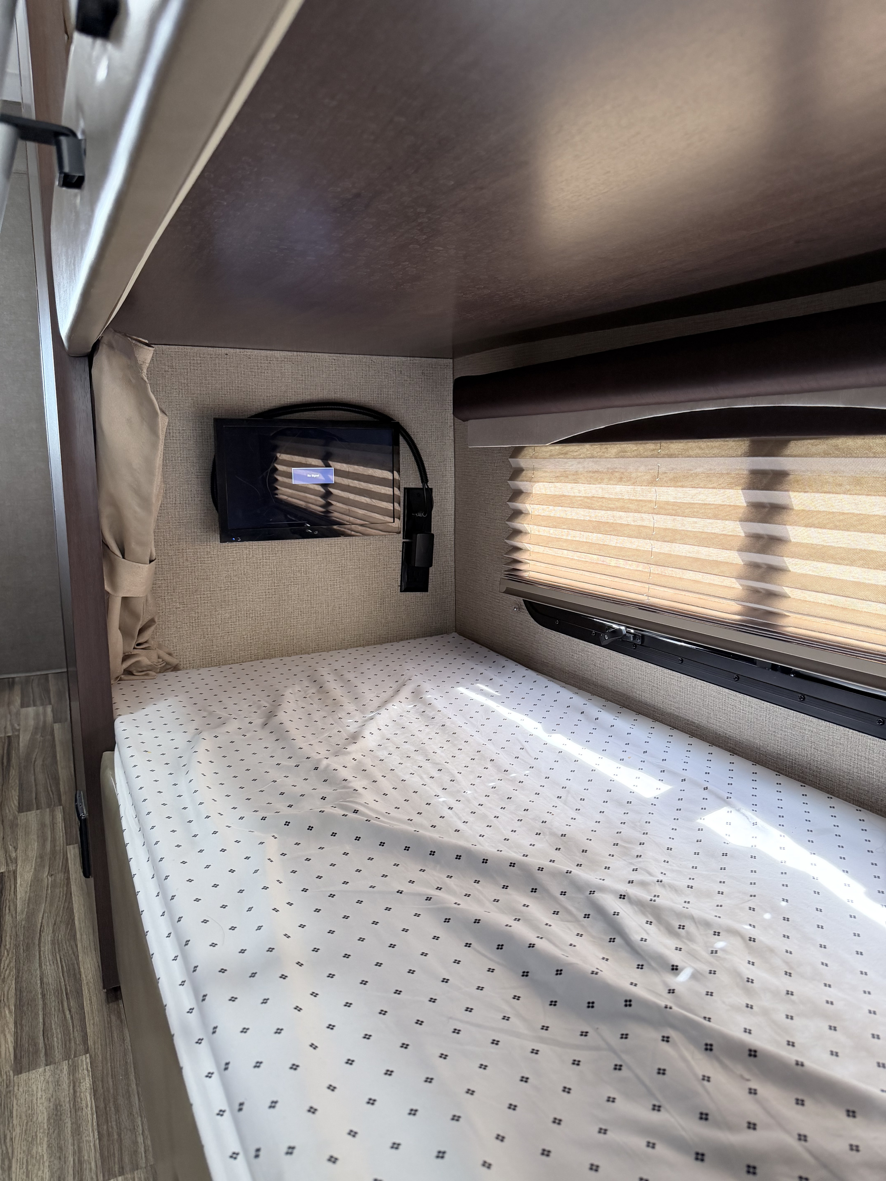 Cozy bunk bed inside an rv rental, featuring a wall-mounted TV (no signal), patterned bedding, and a window with blinds.. Thor A.C.E. 2018