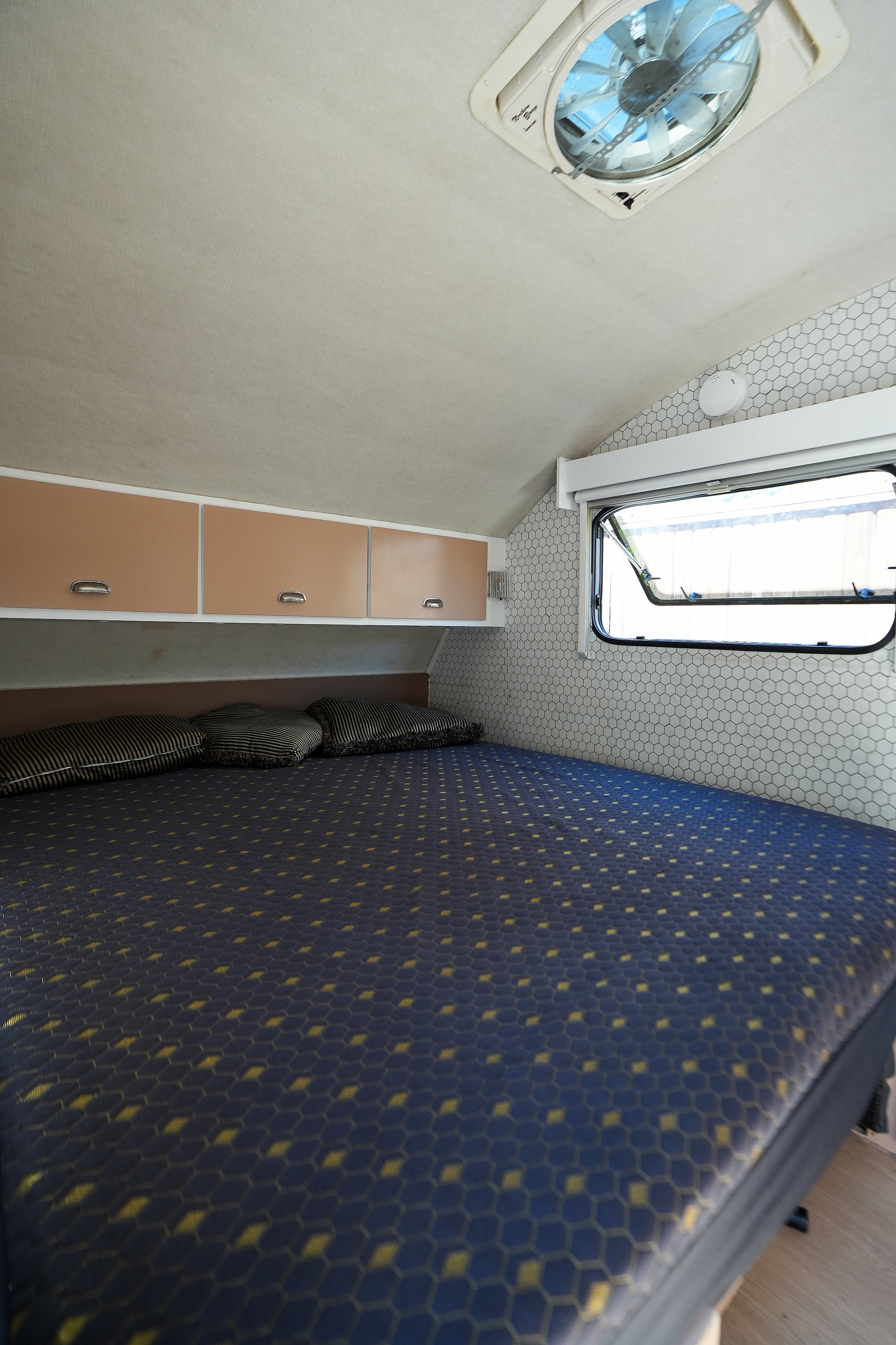 Cozy rv rental bedroom interior featuring a patterned bed, overhead cabinets, a window with a view, and a ceiling vent.. Thor TAB Trailer 2005
