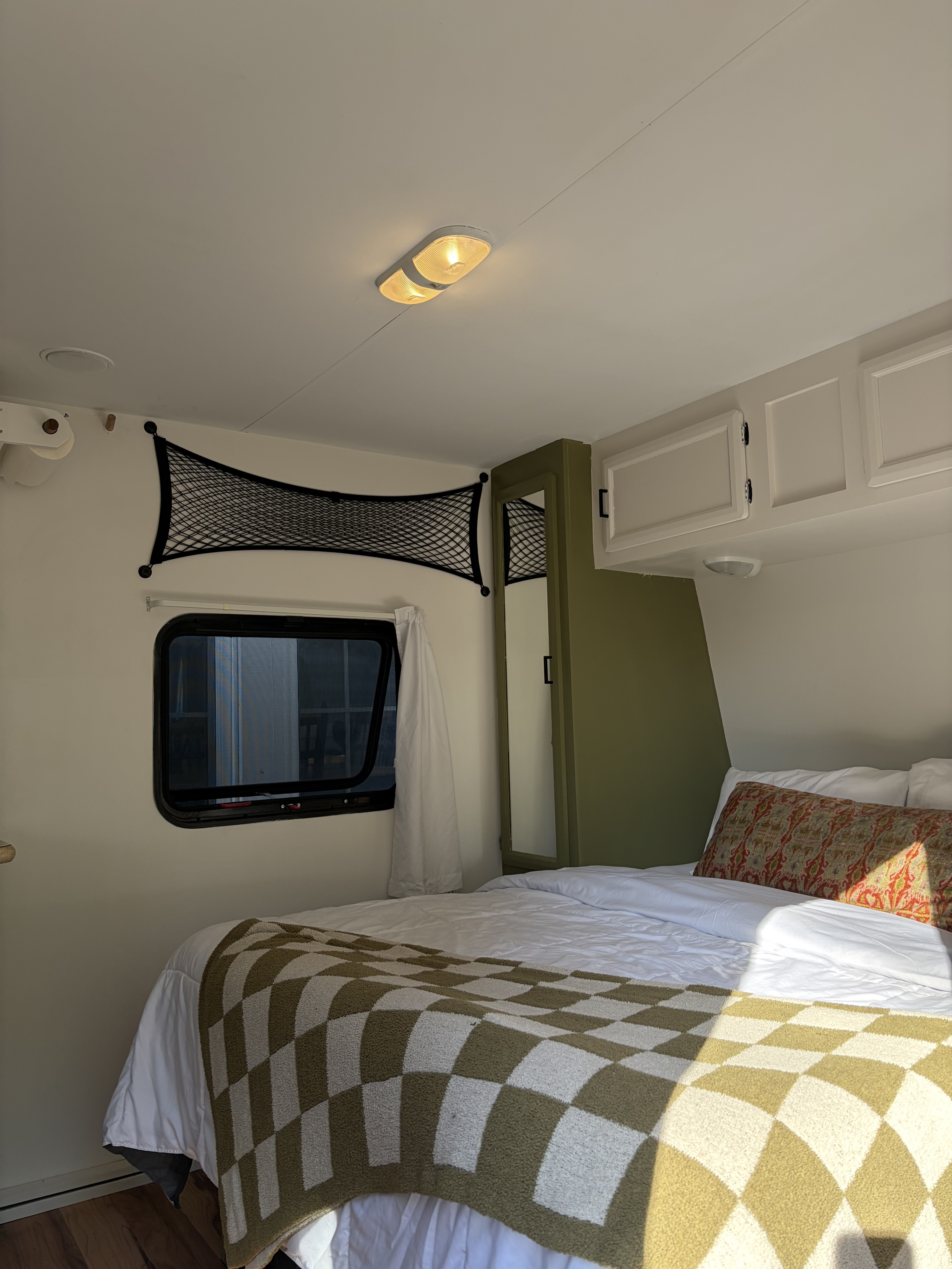 Cozy rv rental bedroom interior featuring a bed with a green checkered blanket, window, overhead cabinets, and olive accents.. KZ Sportsmen 2011