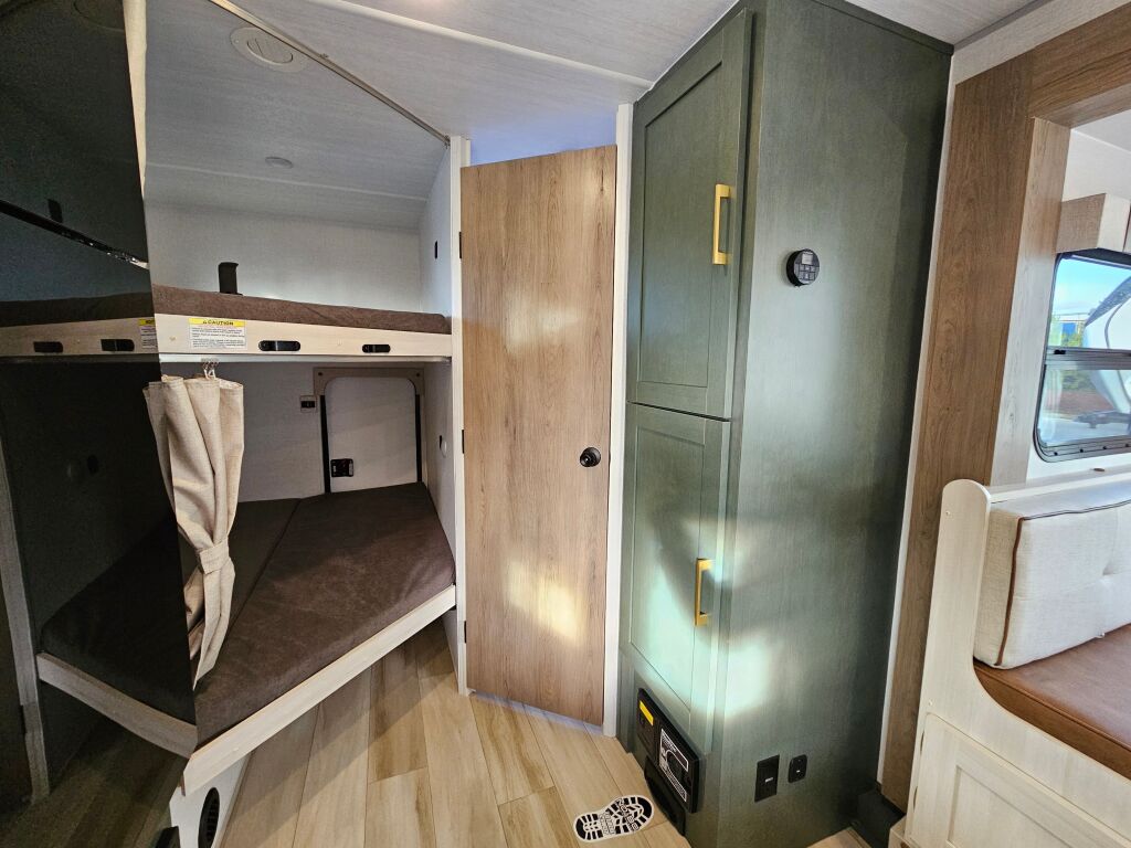 Cozy RV rental interior with bunk beds, a large green storage cabinet, and comfortable seating by a window, ready for travel.. Forest River No Boundaries NB20.3 2026