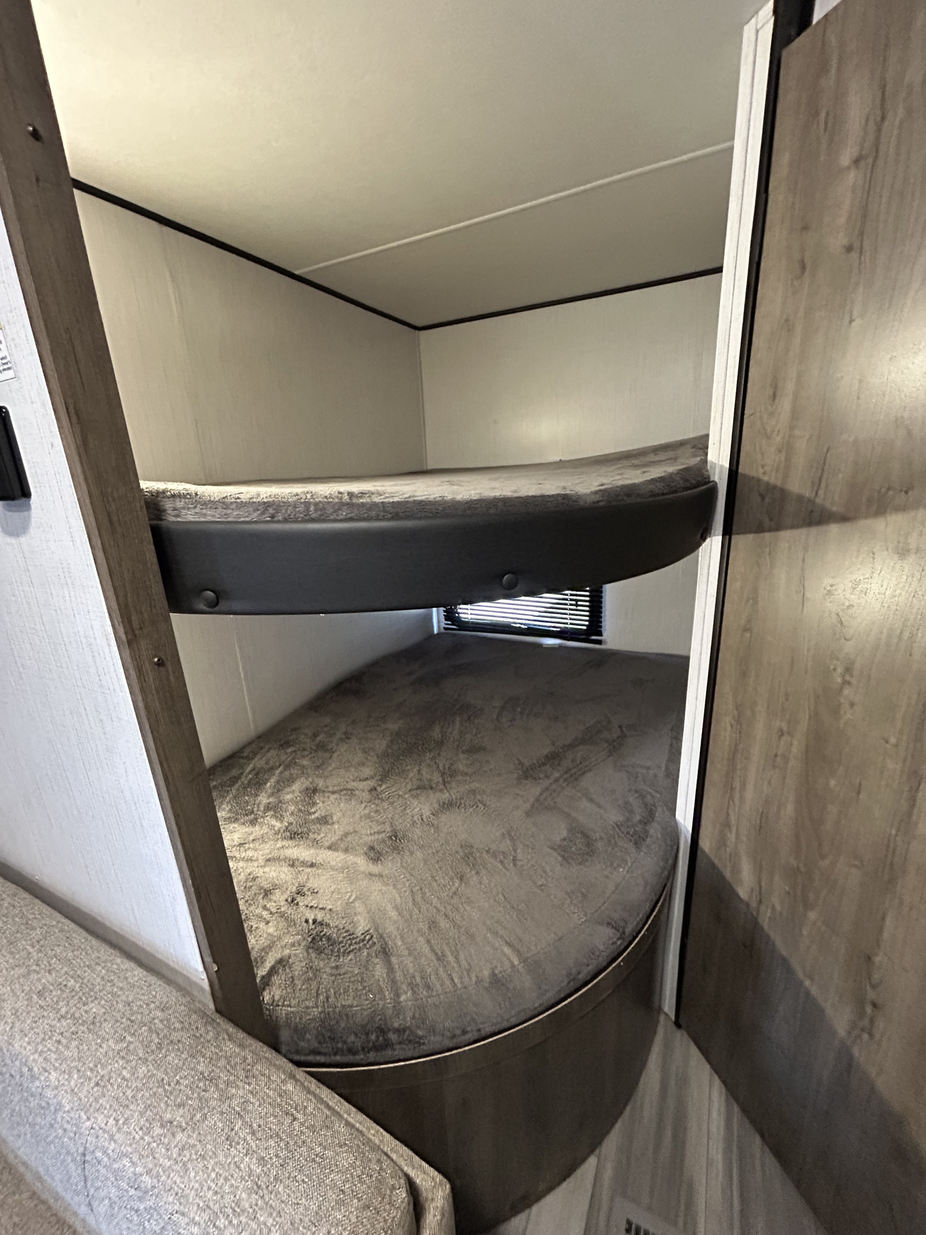 Inside an RV rental, two bunk beds with gray mattresses and a small window offer comfy sleeping. Perfect for family road trips.. Heartland RVs Pioneer 2022