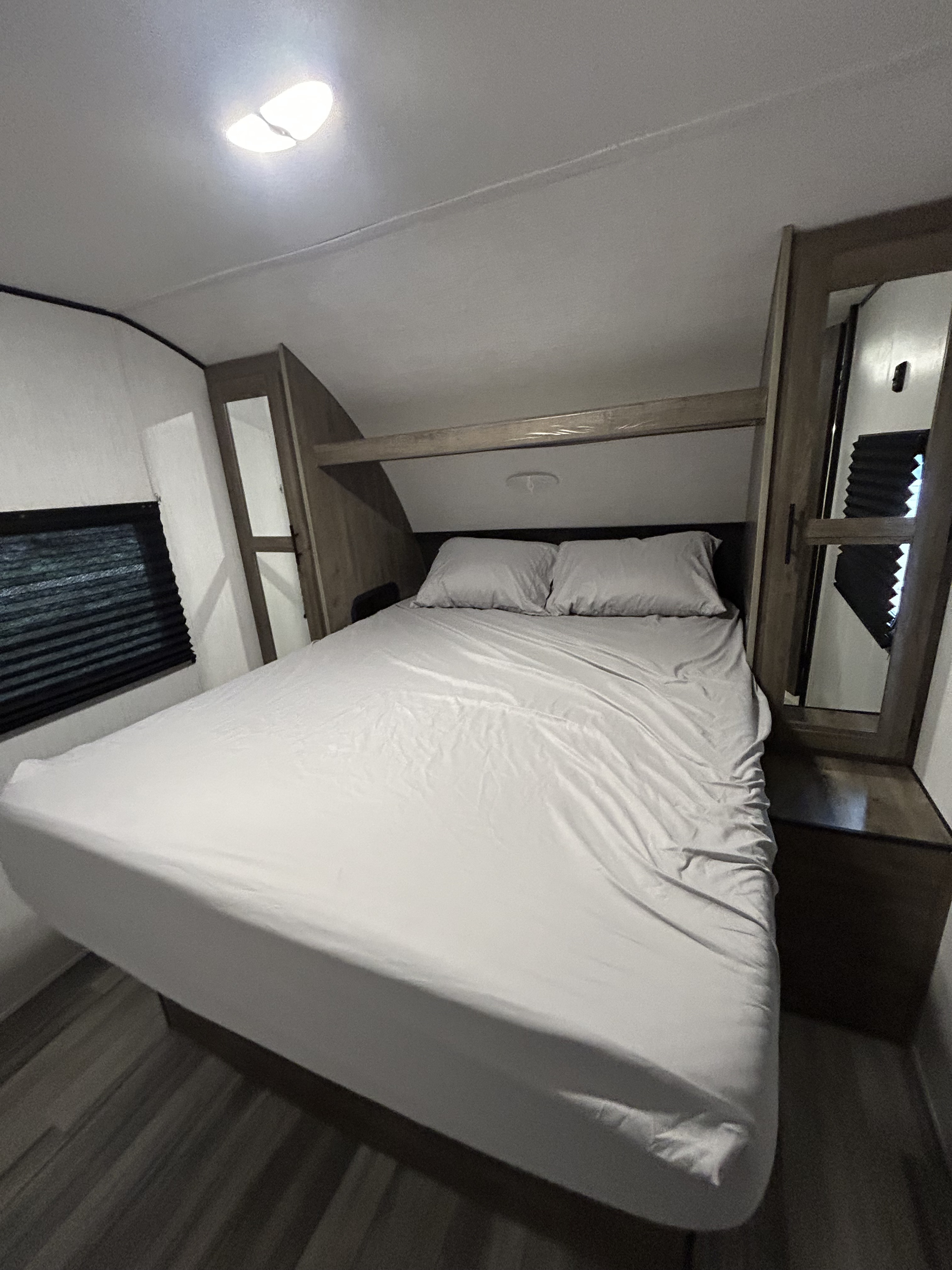 Cozy RV rental bedroom with a comfortable bed, window, and overhead storage, offering practical mobile accommodations.. Heartland RVs Pioneer 2022