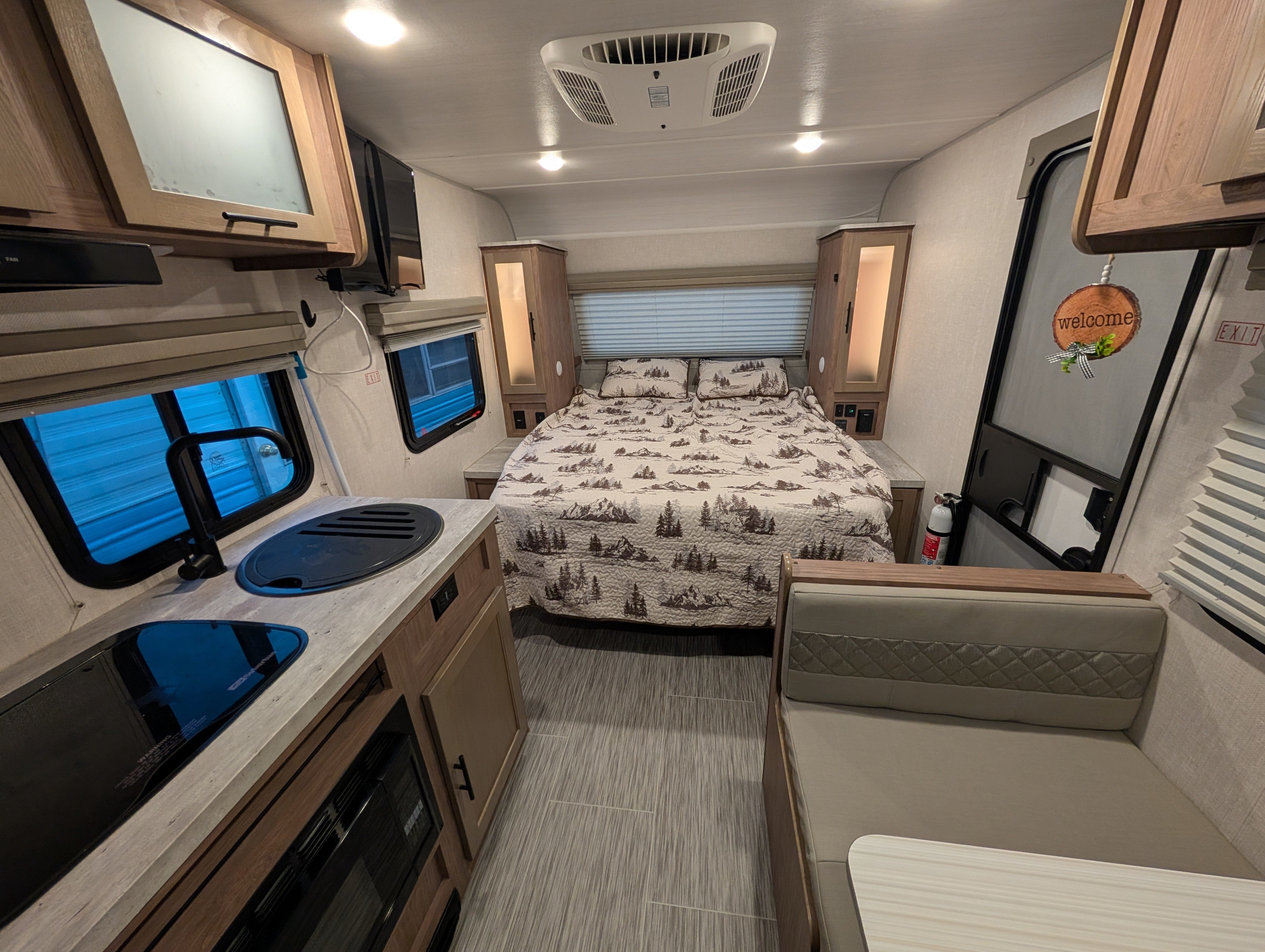 Cozy RV rental interior with kitchen, bed with scenic quilt, dinette, and overhead cabinets. A functional and inviting space.. No Boundaries 19 2022