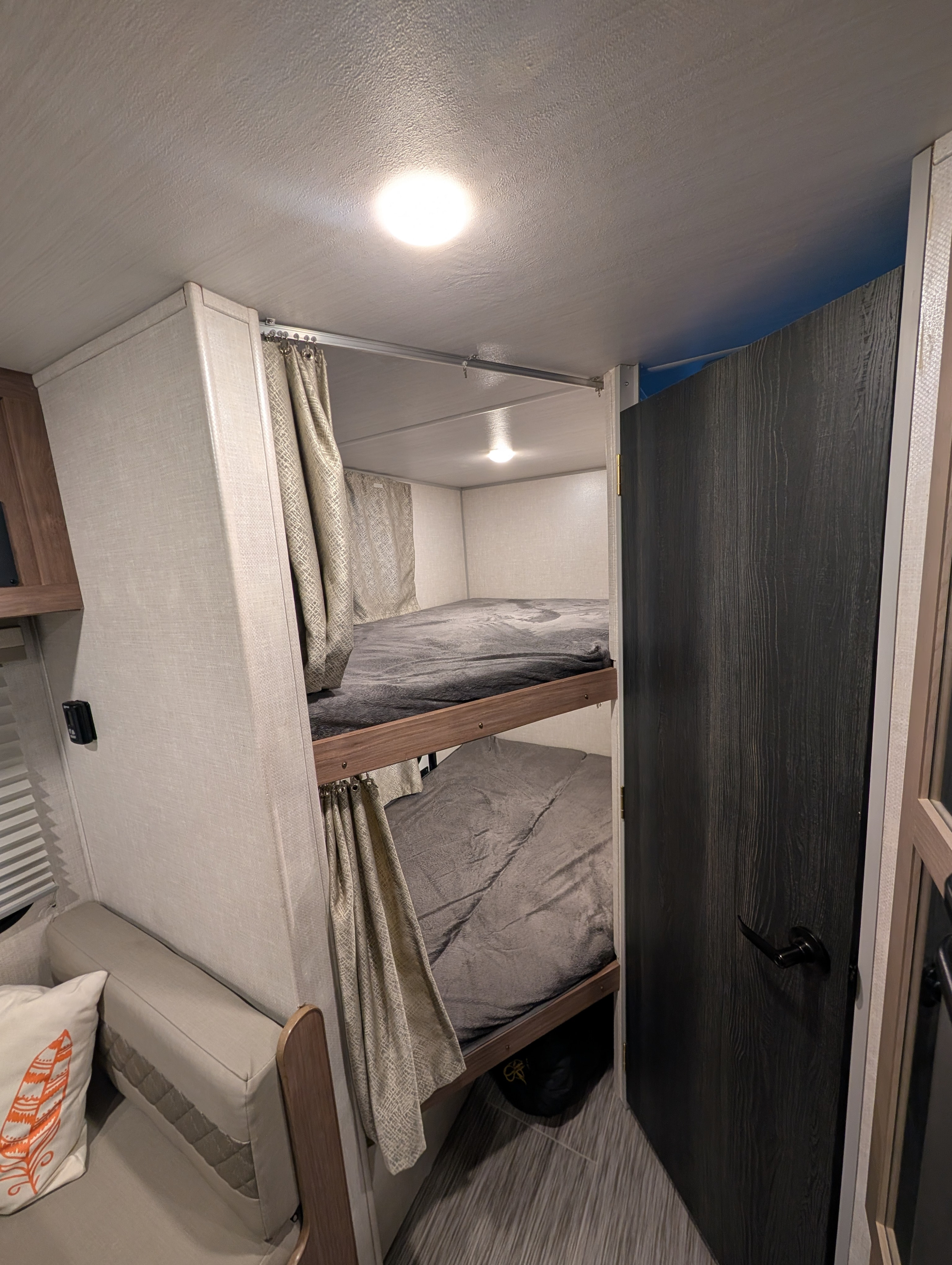 RV rental interior: stacked bunk beds with privacy curtains and soft gray blankets, a cozy sleeping area for travelers.. No Boundaries 19 2022