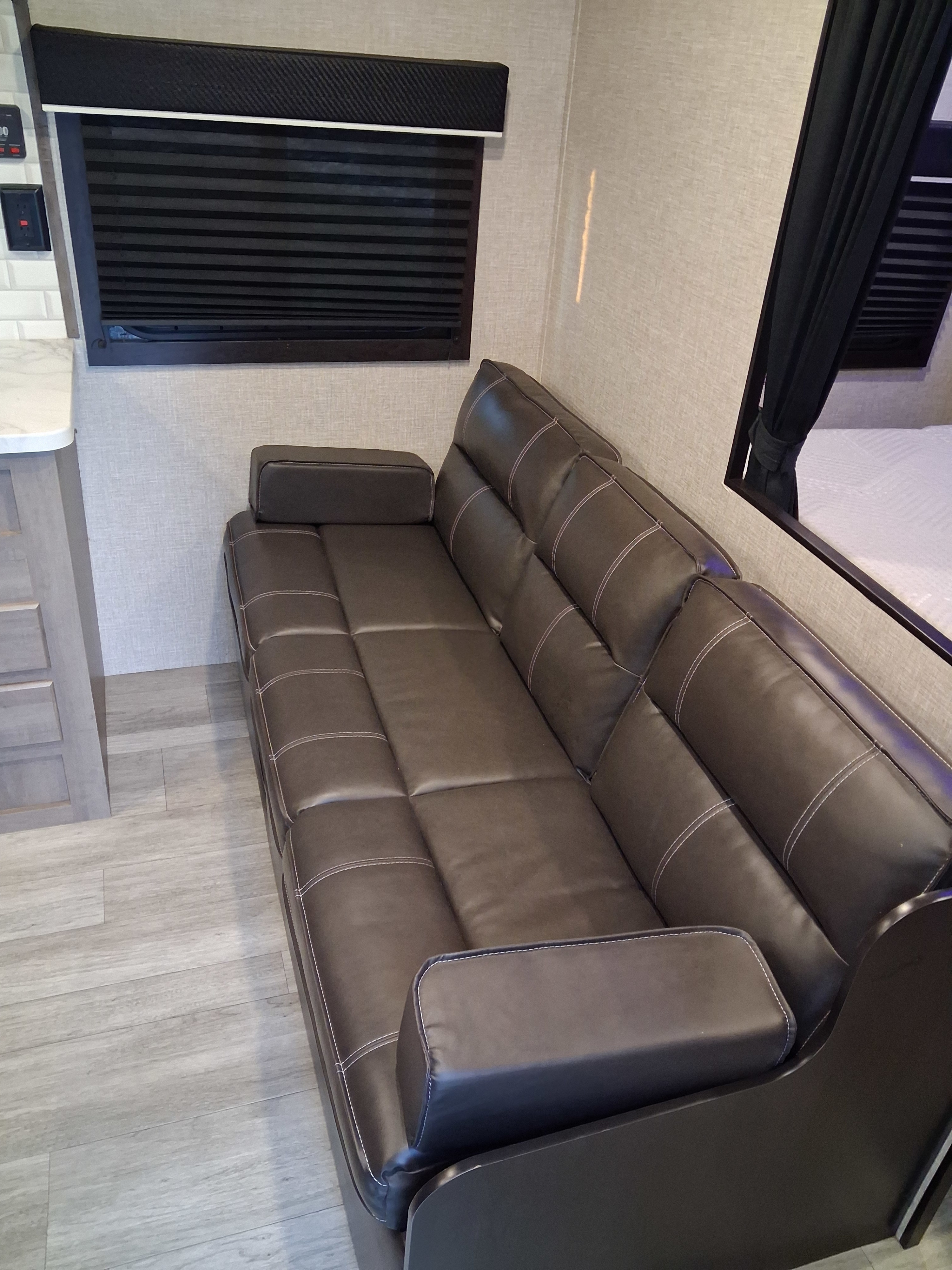Comfortable dark brown sofa, window with black blinds, and light wood flooring in an RV rental interior.. Jayco Jay Flight SLX Rocky Mountain Edition 2022
