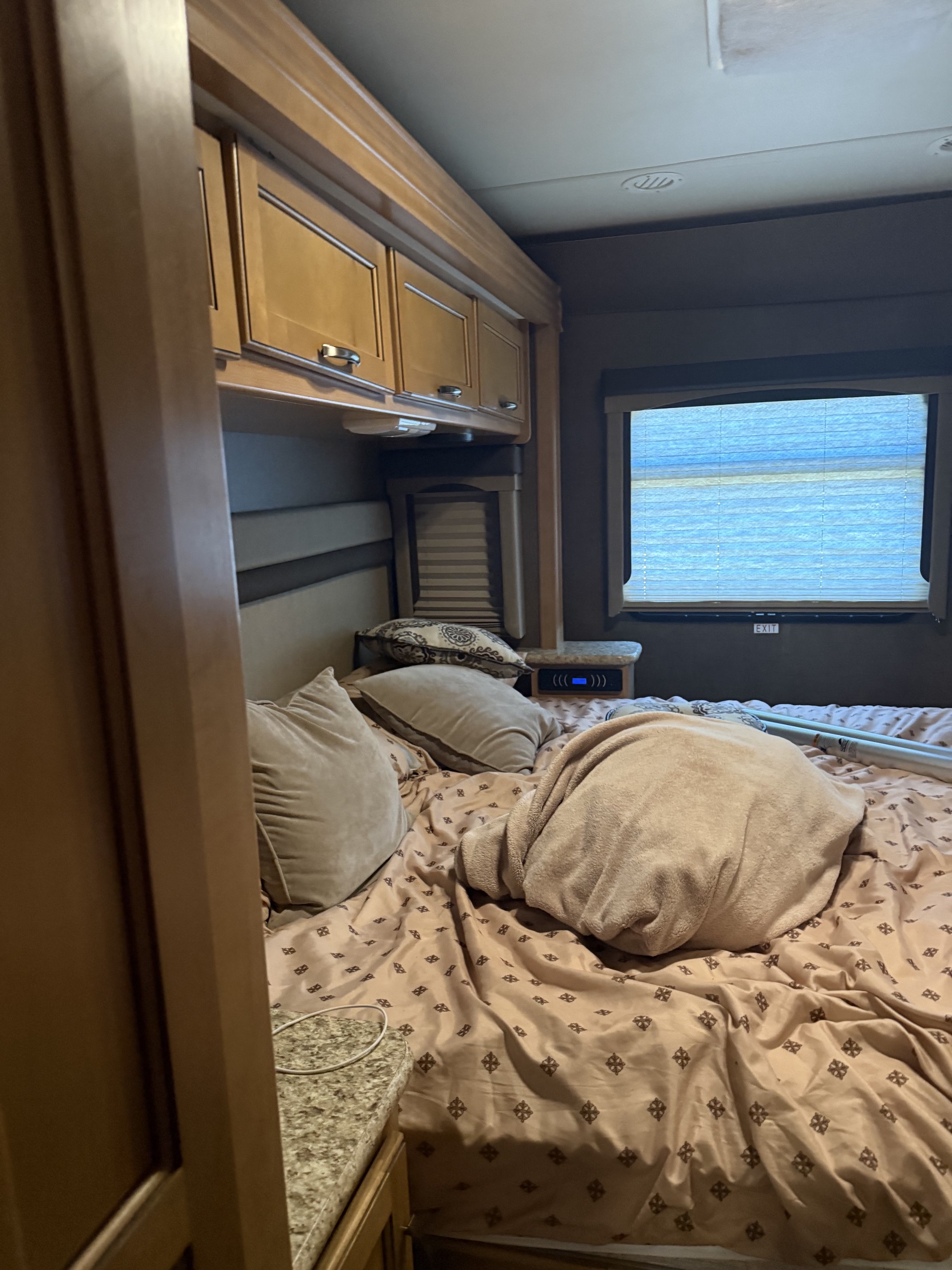 Comfortable RV rental bedroom interior features a cozy bed with pillows, overhead cabinets, and a window. Great for travel.. A.C.E. A.C.E. Motorhome 2015