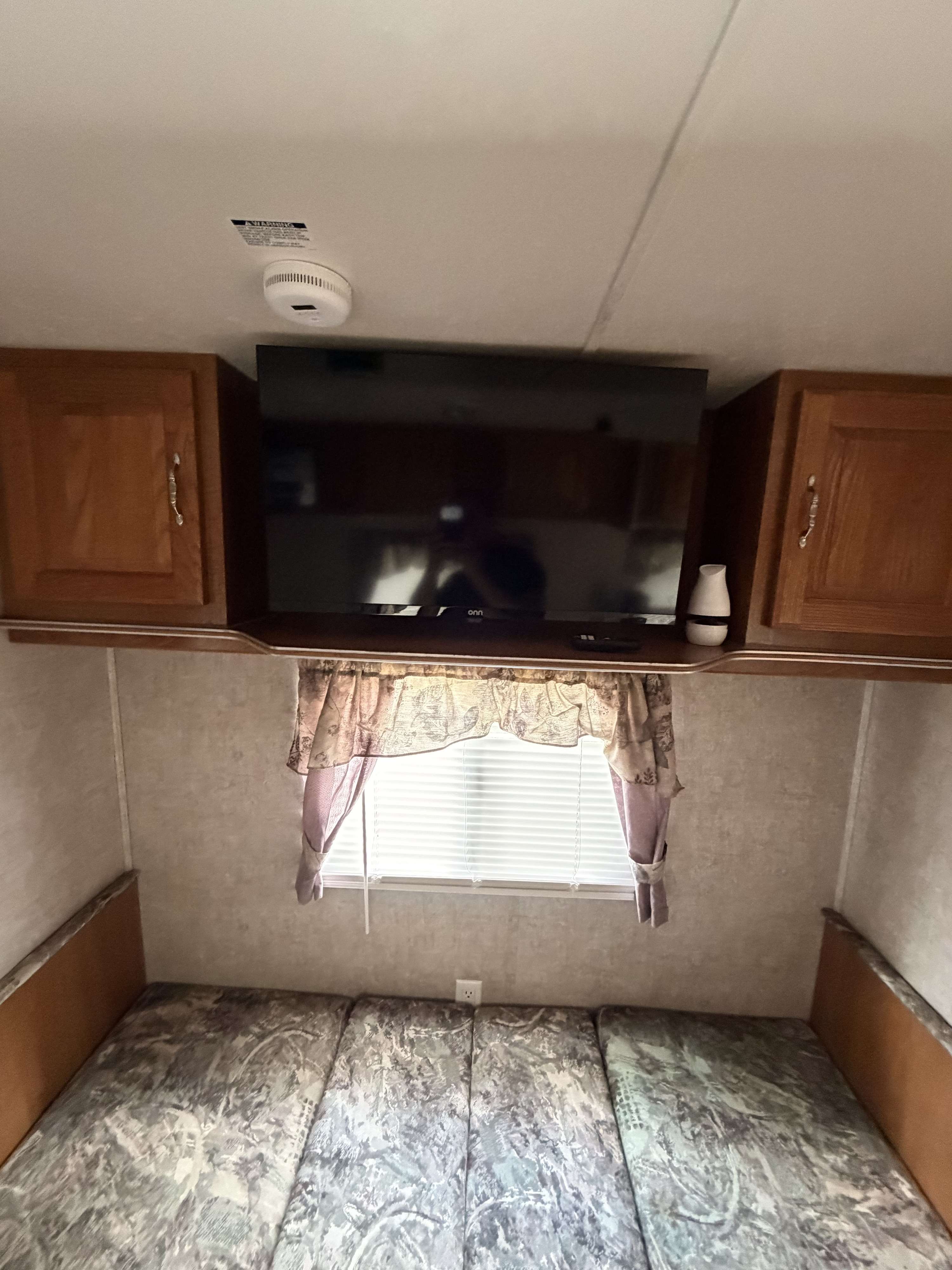 Inside an RV rental: a compact sleeping area with an overhead TV, storage cabinets, window, and patterned cushions.. Sun Valley Roadrunner XL 2005