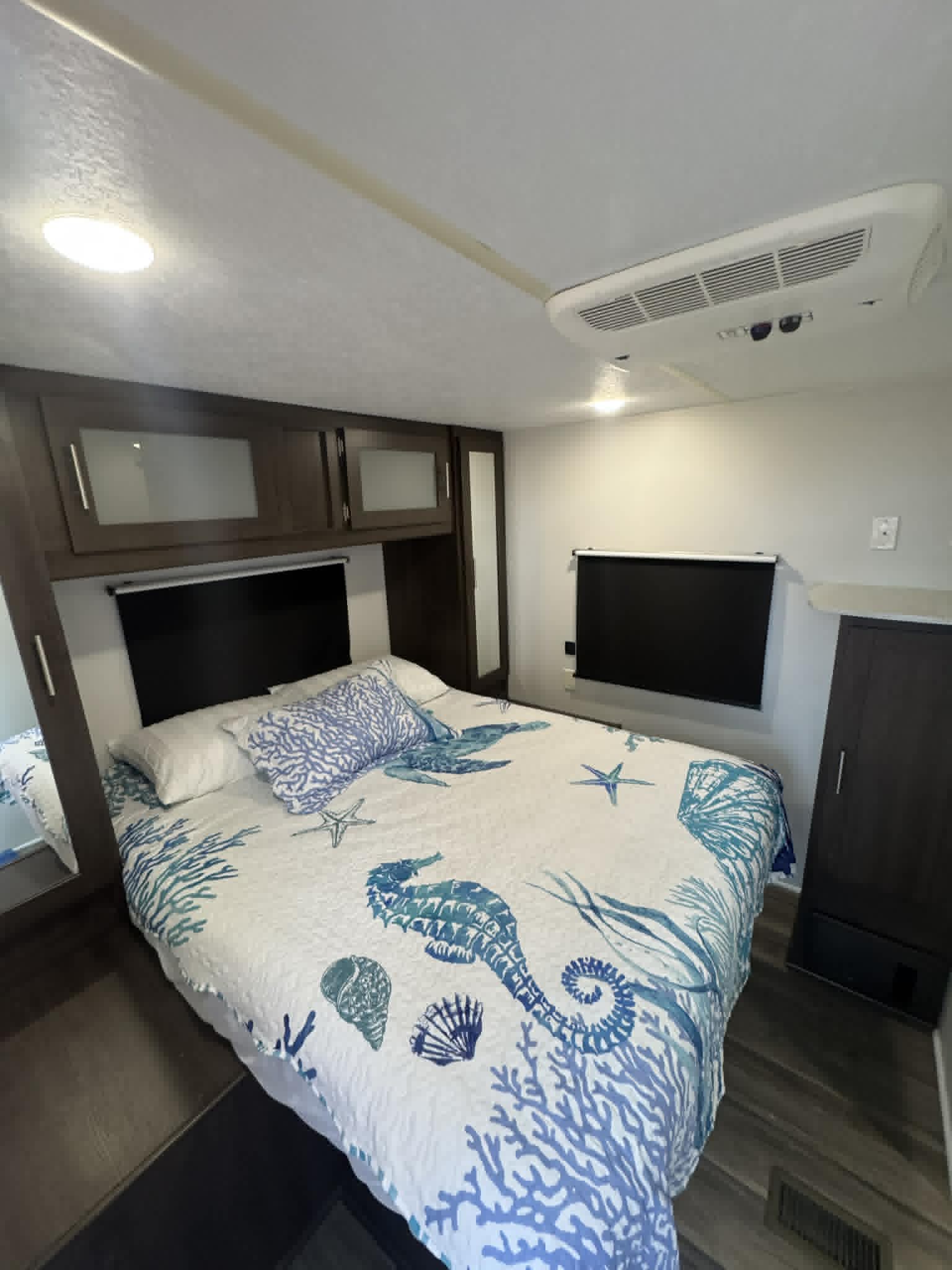 Ocean-themed RV rental bedroom features a bed with blue and white marine bedding, overhead cabinets, and an AC unit.. Forest River Salem 2020