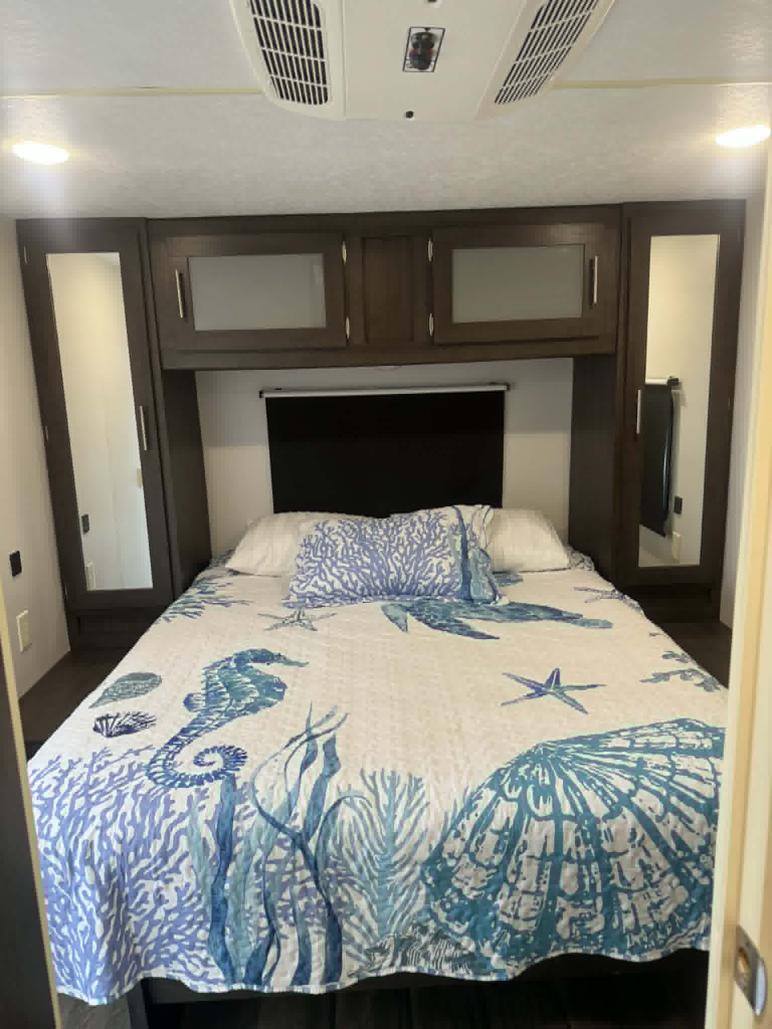 Comfortable RV rental bedroom with an ocean-themed bedspread, mirrored wardrobes, and overhead storage for your travels.. Forest River Salem 2020