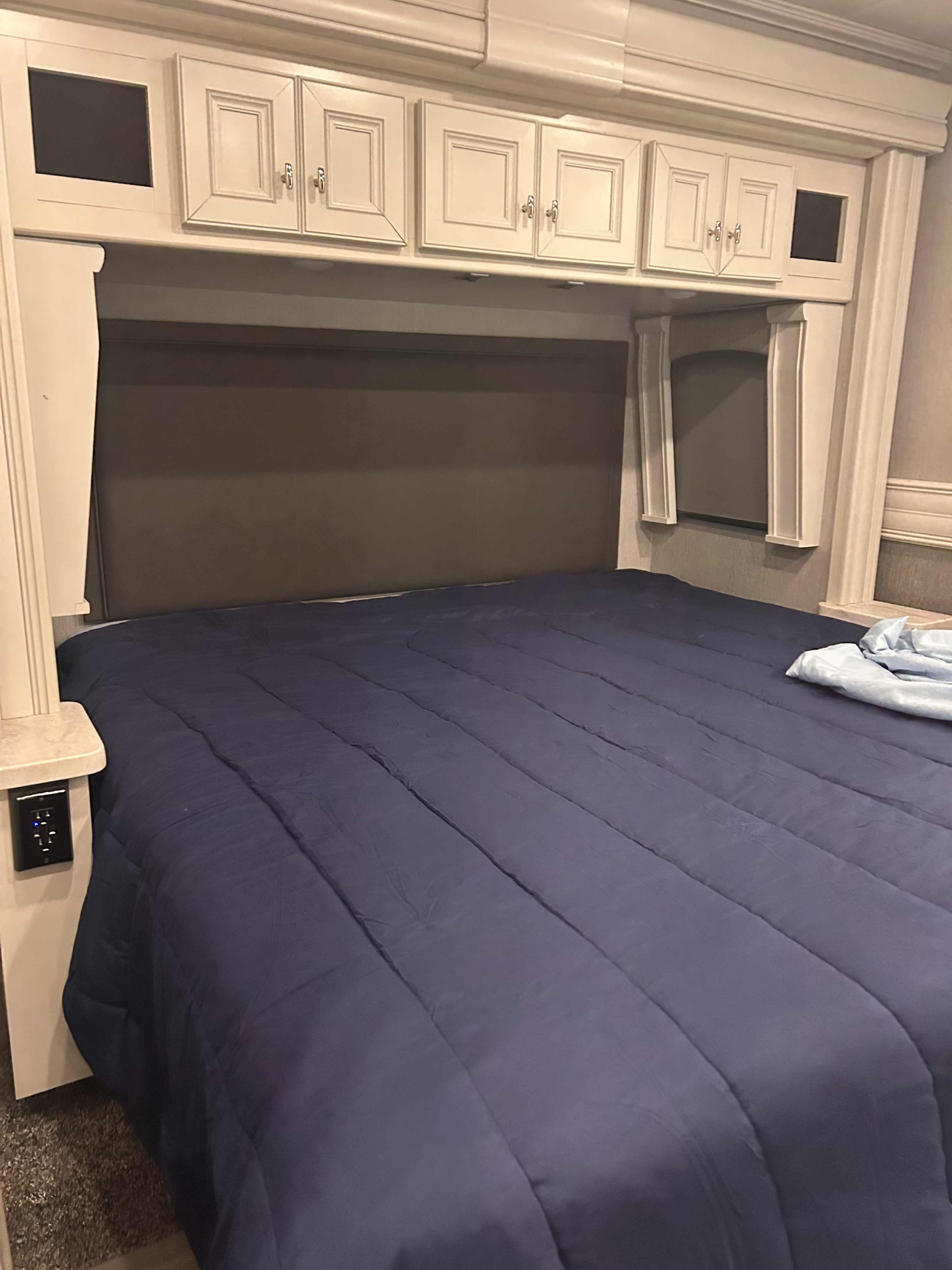 Cozy RV rental bedroom with blue comforter, padded headboard, and overhead cabinets for comfortable travels.. Holiday Rambler Navigator 2022