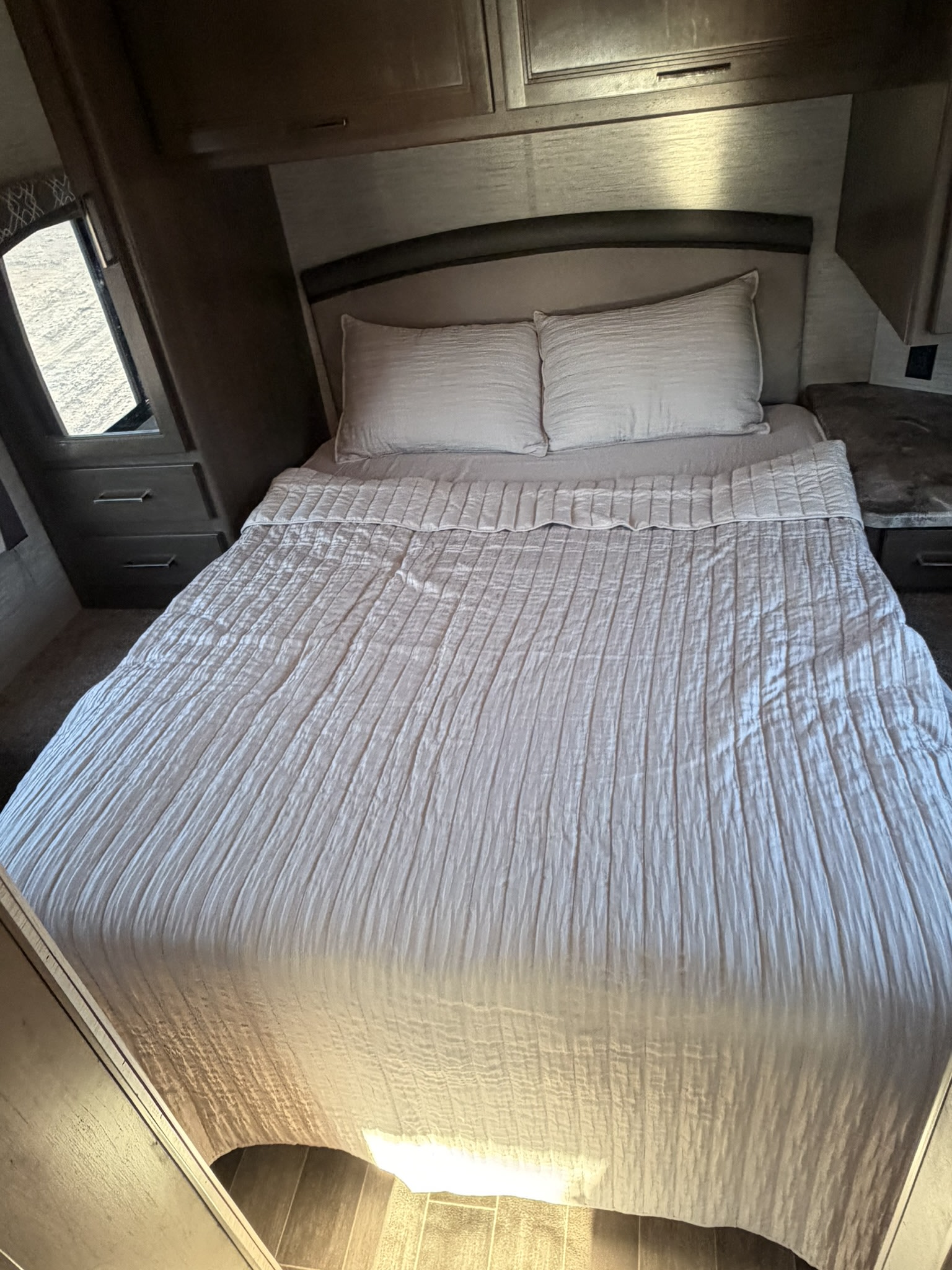 This RV rental bedroom offers a comfortable bed with light, textured comforter, pillows, overhead storage, and a window.. Thor Chateau 2020