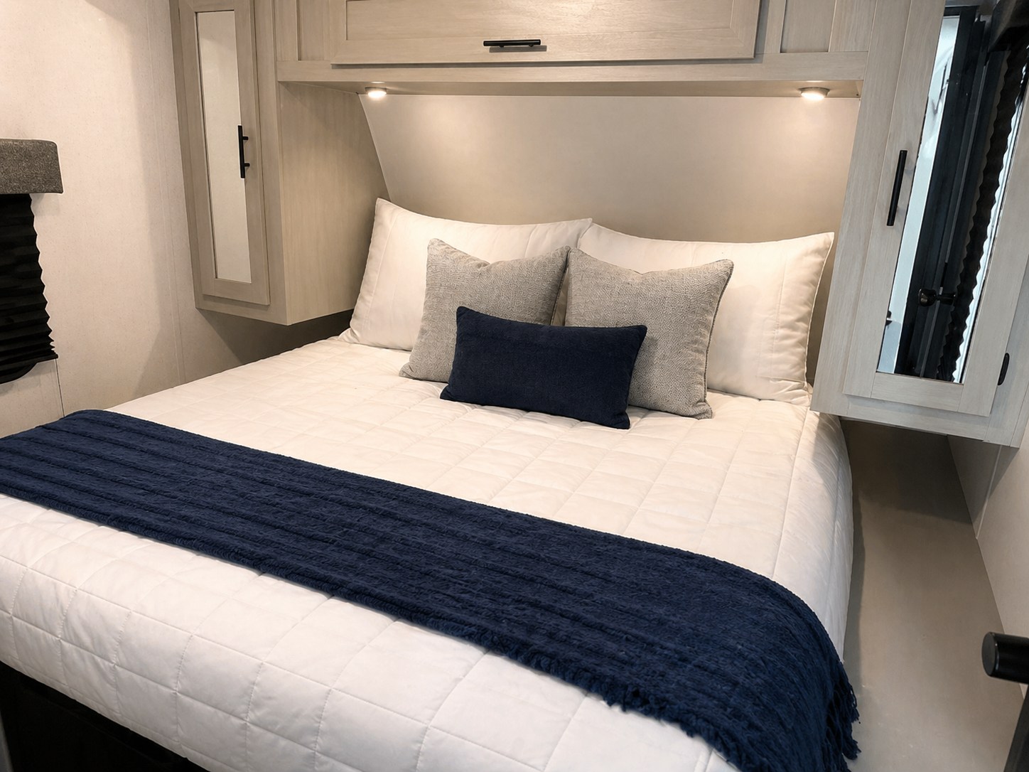 Relaxing RV rental bedroom: a clean white bed with blue and grey pillows, overhead cabinets, and soft lighting for comfort.. Forest River Wildwood FSX 2022