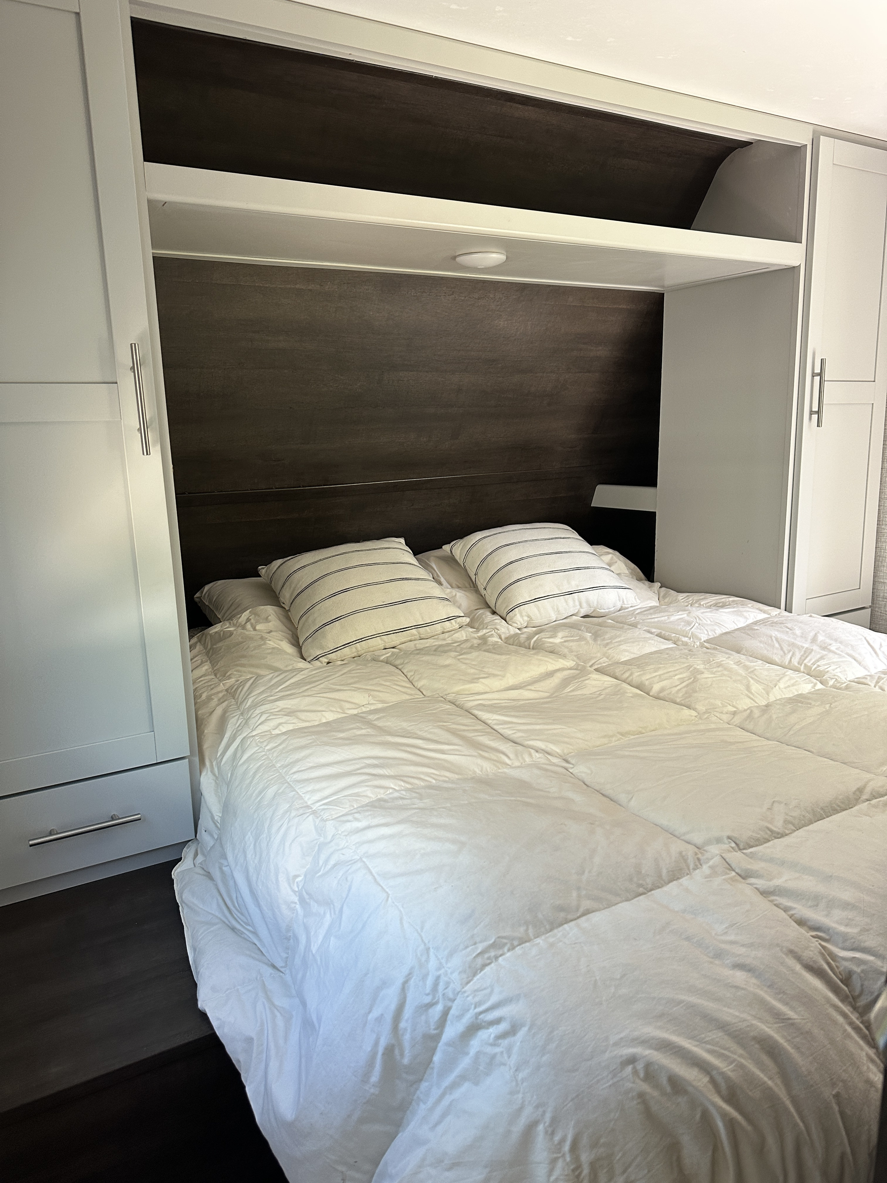Cozy RV rental bedroom features a built-in bed with white bedding, striped pillows, and dark wood accents.. Keystone RV Bullet Crossfire 2021