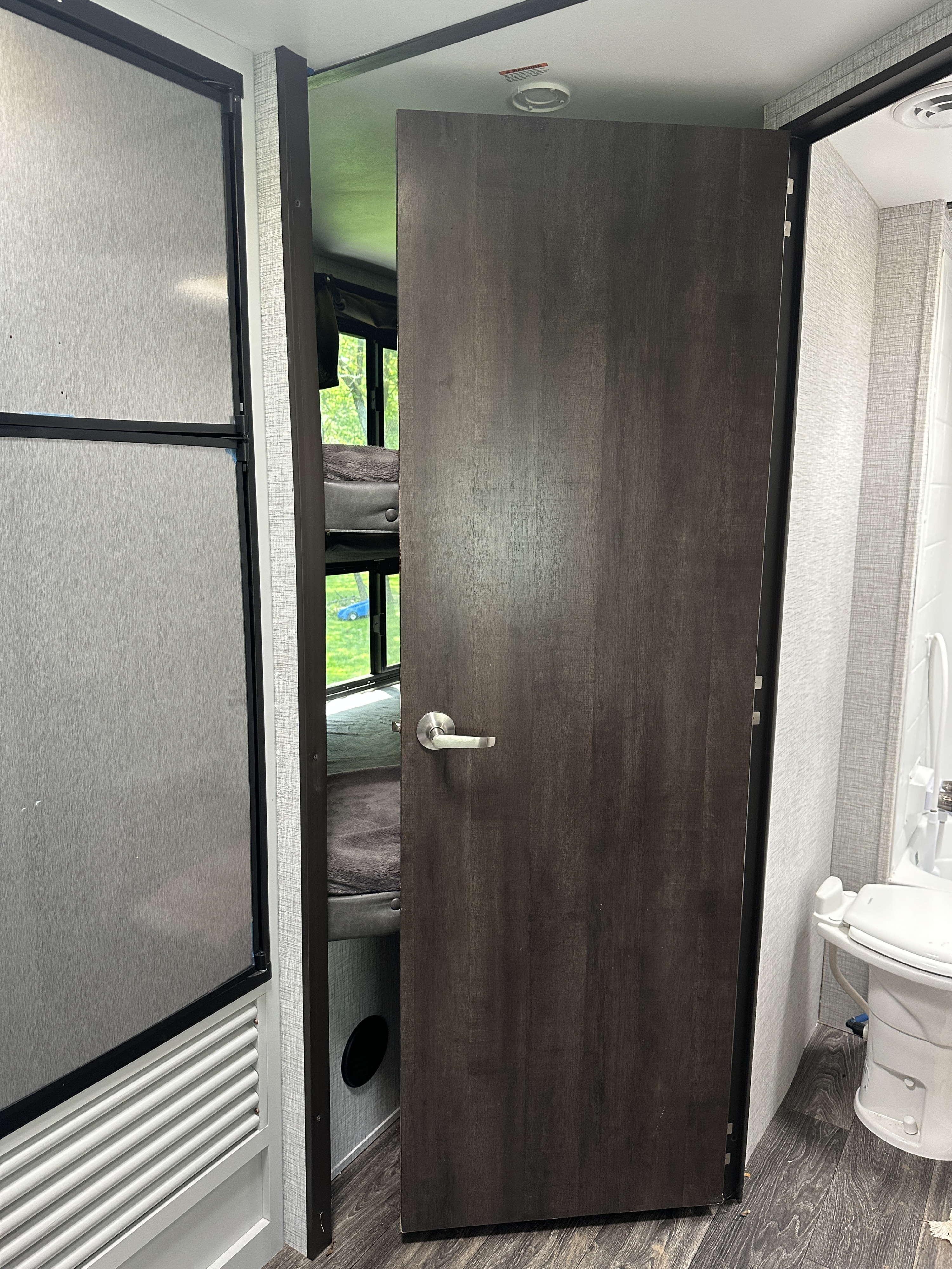 RV rental interior featuring a fridge, open door revealing bunk beds, and bathroom door with toilet visible.. Keystone RV Bullet Crossfire 2021