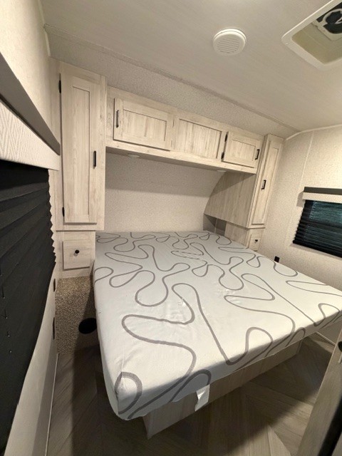Discover this cozy RV rental bedroom: a bright space with a patterned bed, overhead cabinets, and bedside storage.. Forest River Della Terra 2022