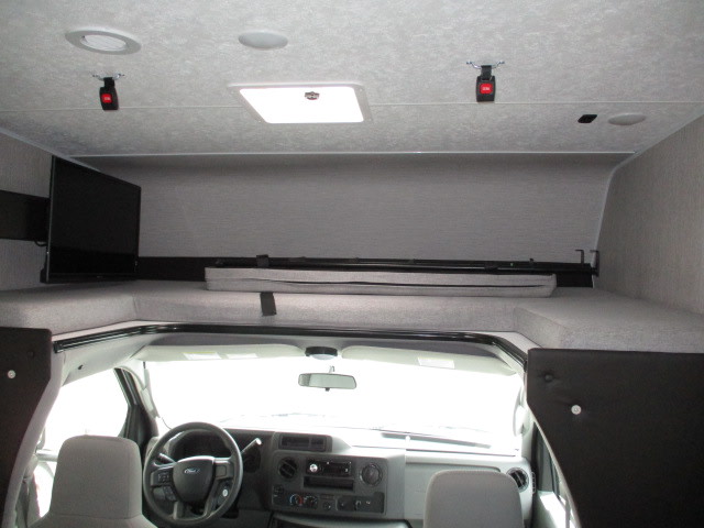 RV rental interior: This motorhome shows an over-cab bunk bed with mattresses, a mounted TV, and the vehicle's driver cabin.. Coachmen Freelander 2022