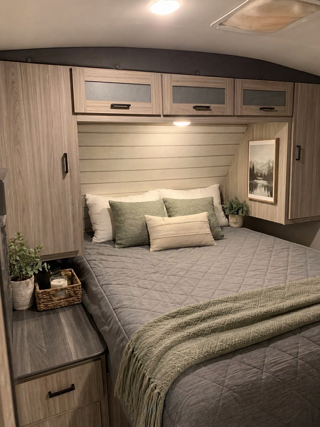 Stylish RV rental bedroom: cozy bed with grey comforter & green throw, modern wood cabinets, & wall decor.. Keystone RV Passport 2022