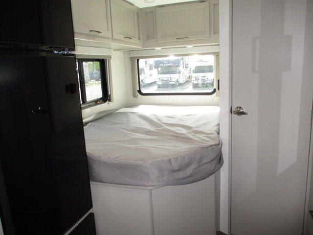 RV rental bedroom interior: a bed with white bedding, windows, light-colored cabinets, and a door to the right.. Thor Motor Coach Four Winds 2026