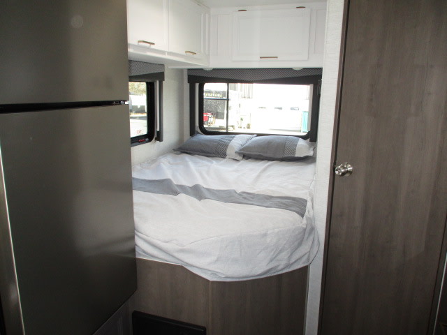 RV rental: Cozy bedroom featuring a bed with gray bedding, large windows, white overhead cabinets, and a partial stainless steel fridge.. Thor Motor Coach Four Winds 2024