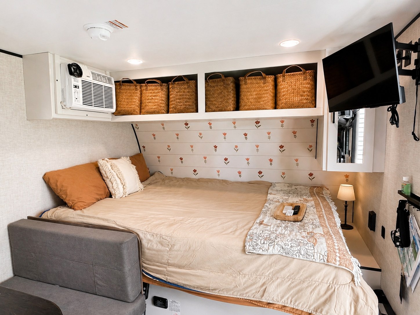 Cozy RV rental bedroom showing a bed, AC, TV, and overhead storage with baskets. Floral wall adds style for travel comfort.. Jayco Jay Flight SLX 2025