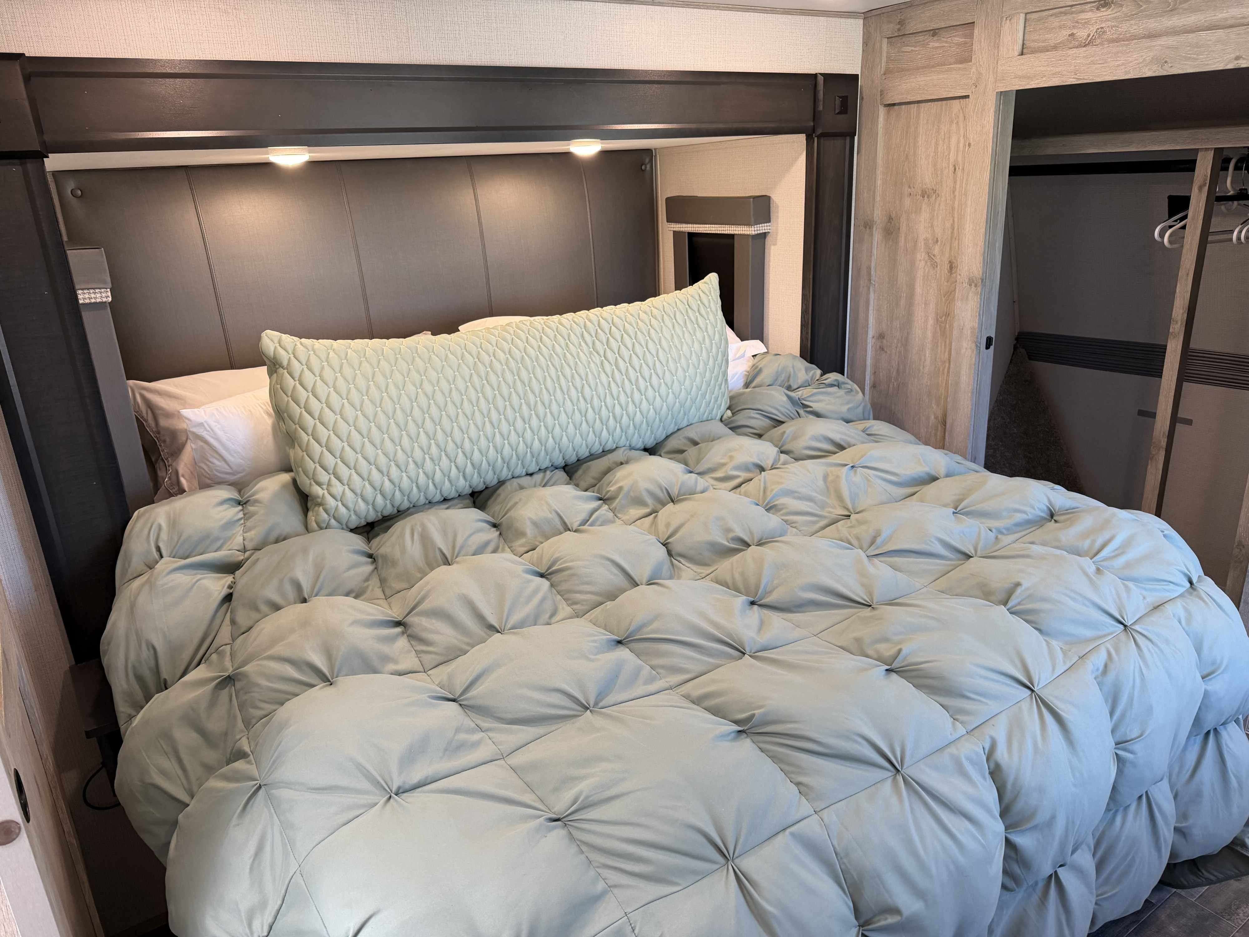 Cozy RV rental bedroom featuring a plush sage green comforter, upholstered headboard with lighting, and a built-in closet for travel.. Keystone RV Avalanche 2022
