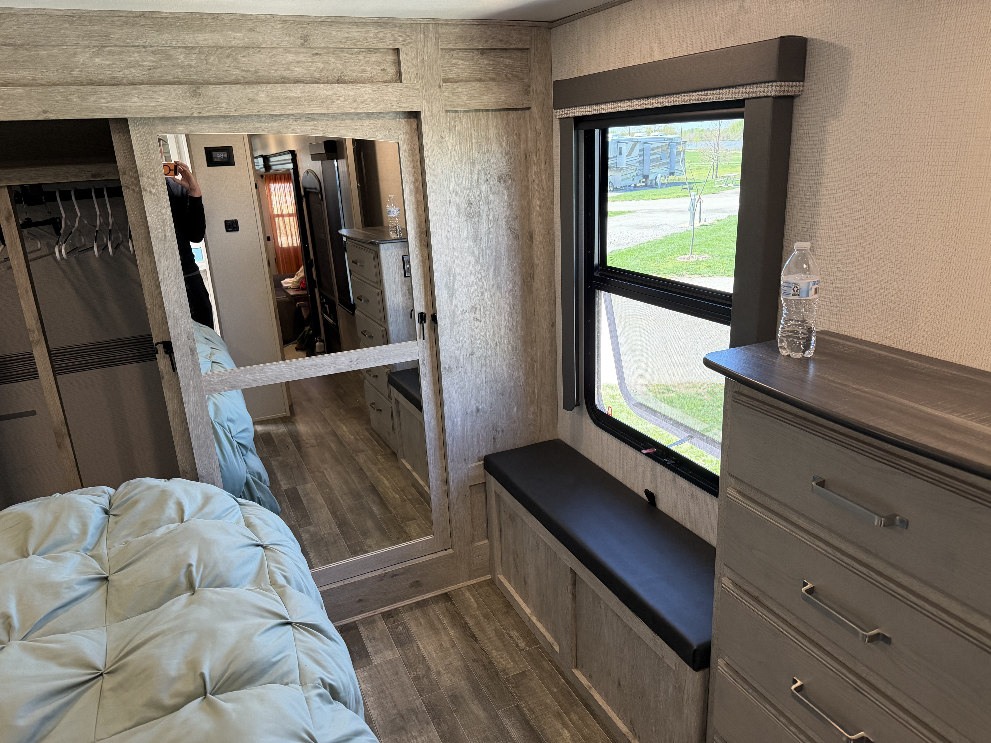 Interior of an RV rental bedroom with light wood cabinetry, a comfortable bed, window view, and a mirrored closet door.. Keystone RV Avalanche 2022