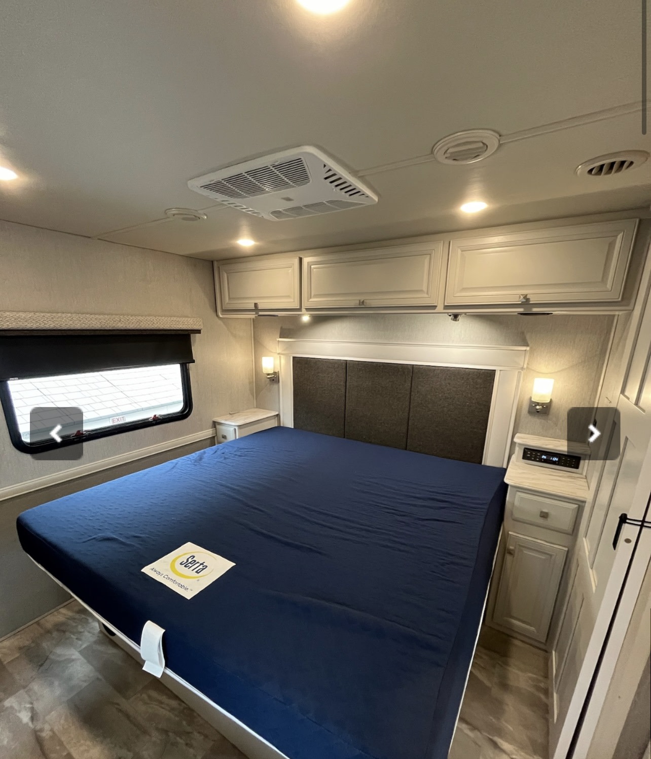 Get comfy in this RV rental bedroom! Features a large bed with a dark blue Serta cover, overhead storage, AC, and bedside tables.. Holiday Rambler Admiral 2021