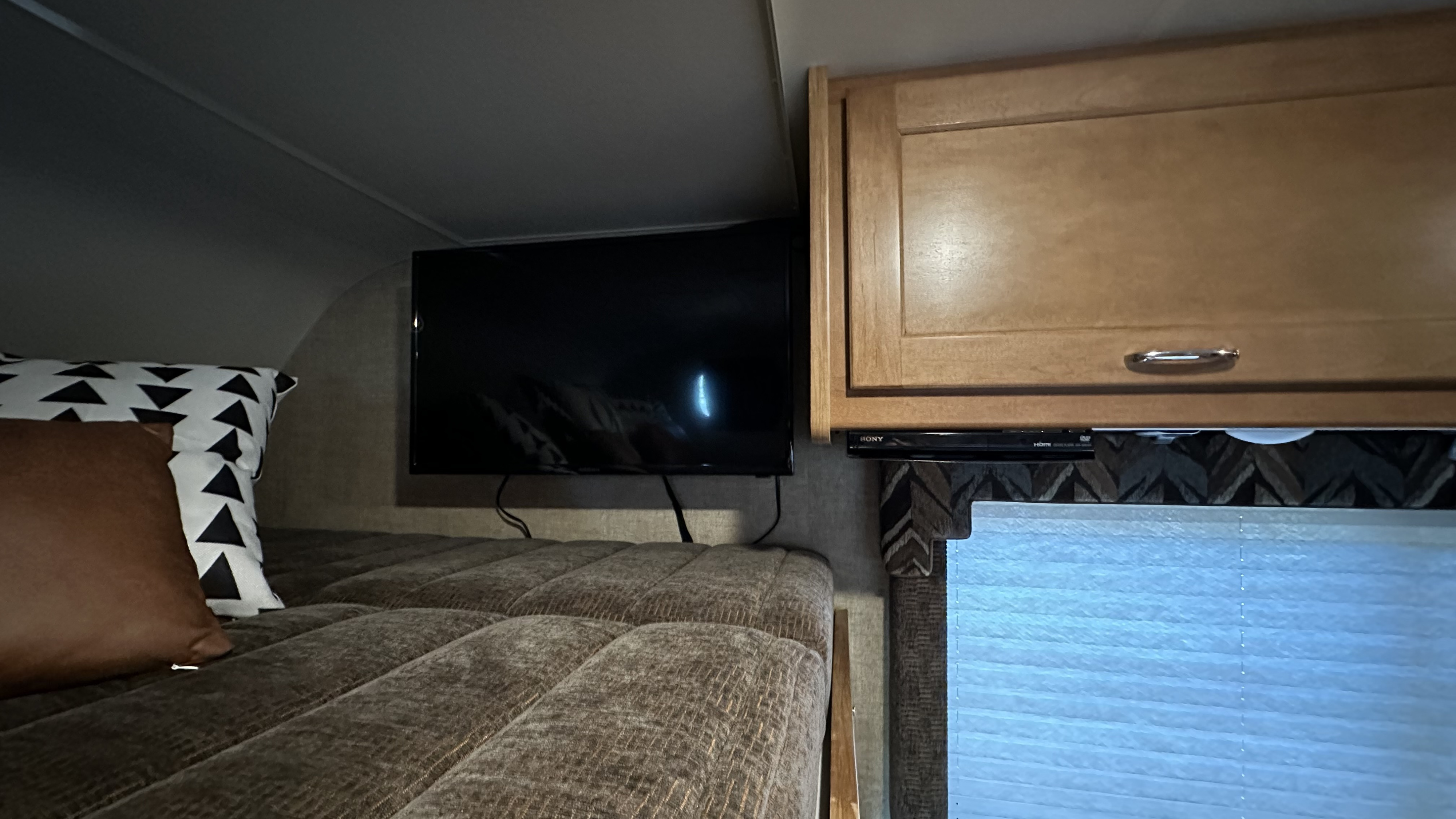 Cozy RV rental interior: A plush bed with decorative pillows, a wall-mounted TV, and wooden cabinets provide comfort and convenience.. Winnebago Minnie Winnie 2018