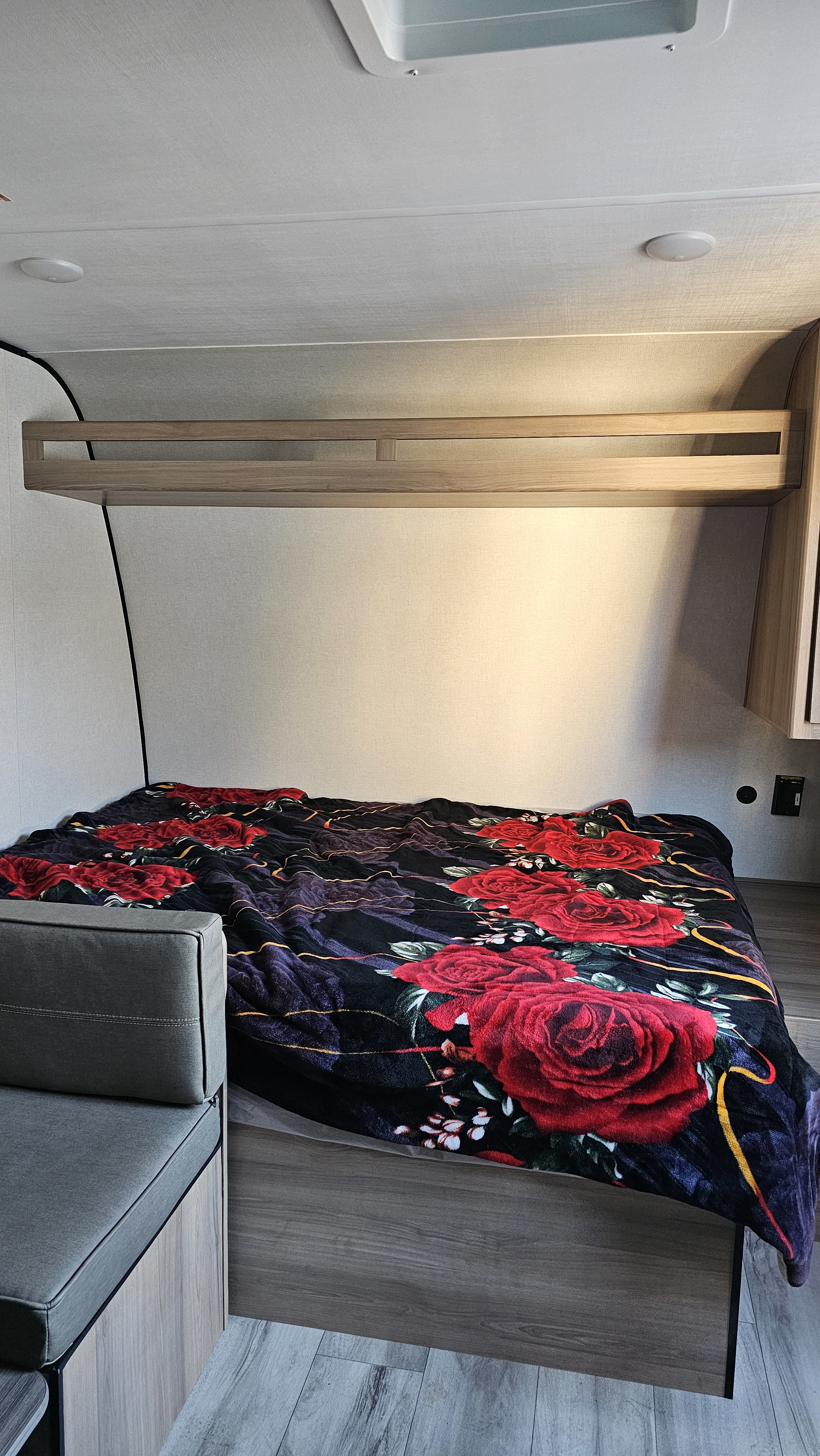 RV rental interior showing a compact bedroom with a bed, vibrant red rose blanket, and practical overhead shelf.. Keystone RV Coleman Light 17Bx 2026