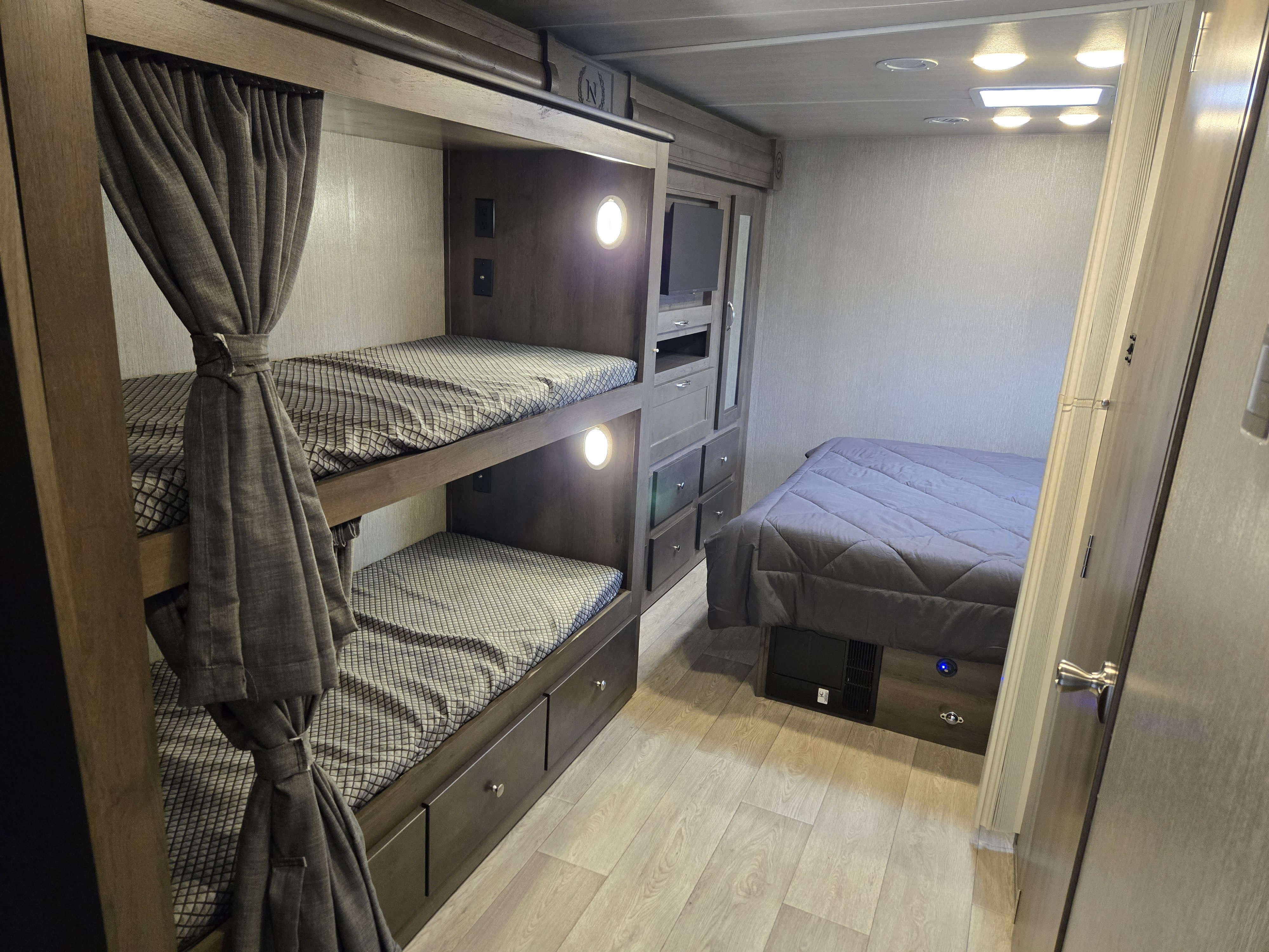 RV rental sleeping area: bunk beds with curtains, a main bed, and central storage, providing compact comfort.. Nexus RV Phantom 2024