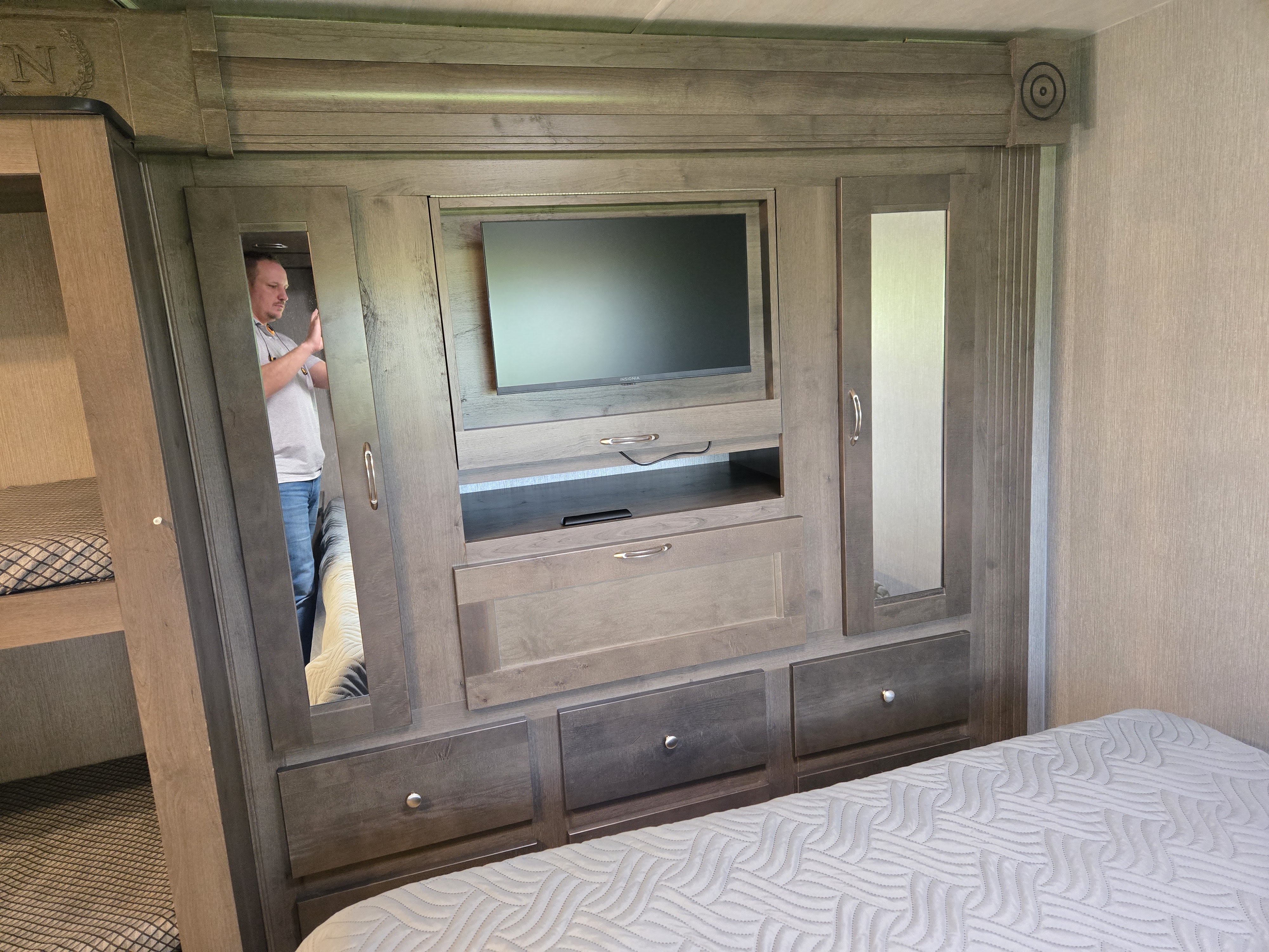 Modern RV rental bedroom interior with a TV, built-in storage, mirrored wardrobes, and a partial view of a bunk bed.. Nexus RV Phantom 2024