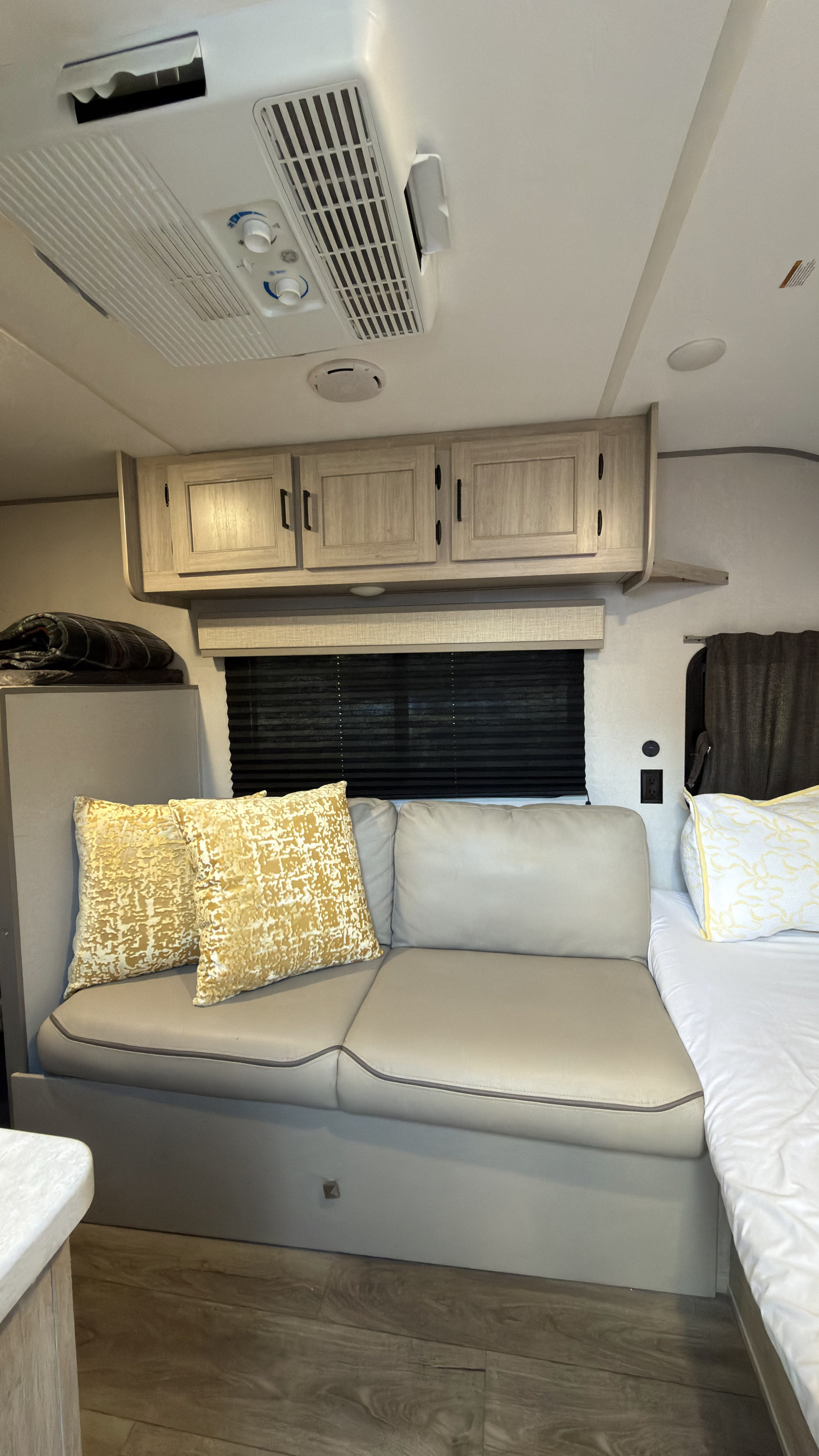 Modern RV rental interior: beige sofa, bed, wood cabinets, AC, and window with blinds. Great for road trips!. Coachmen Catalina Summit Series 7 16bhx 2024