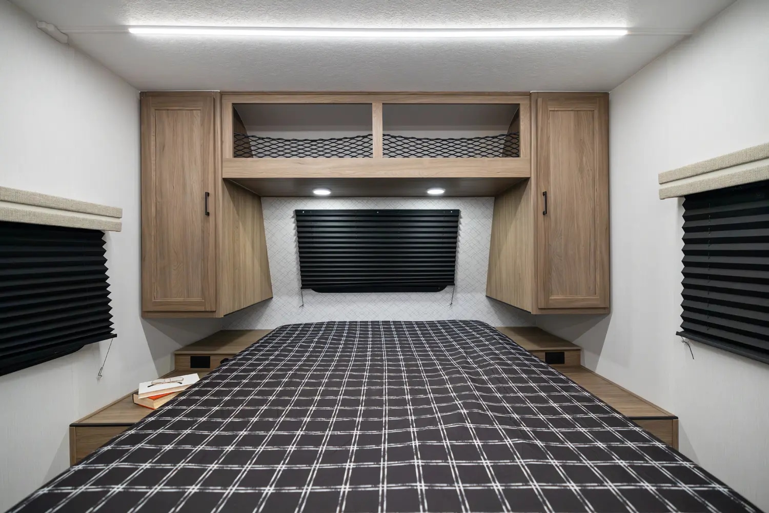 Modern RV rental interior: a functional bedroom featuring a plaid bed, overhead storage, and ambient lighting.. Coachmen Freedom Express 19SE 2025