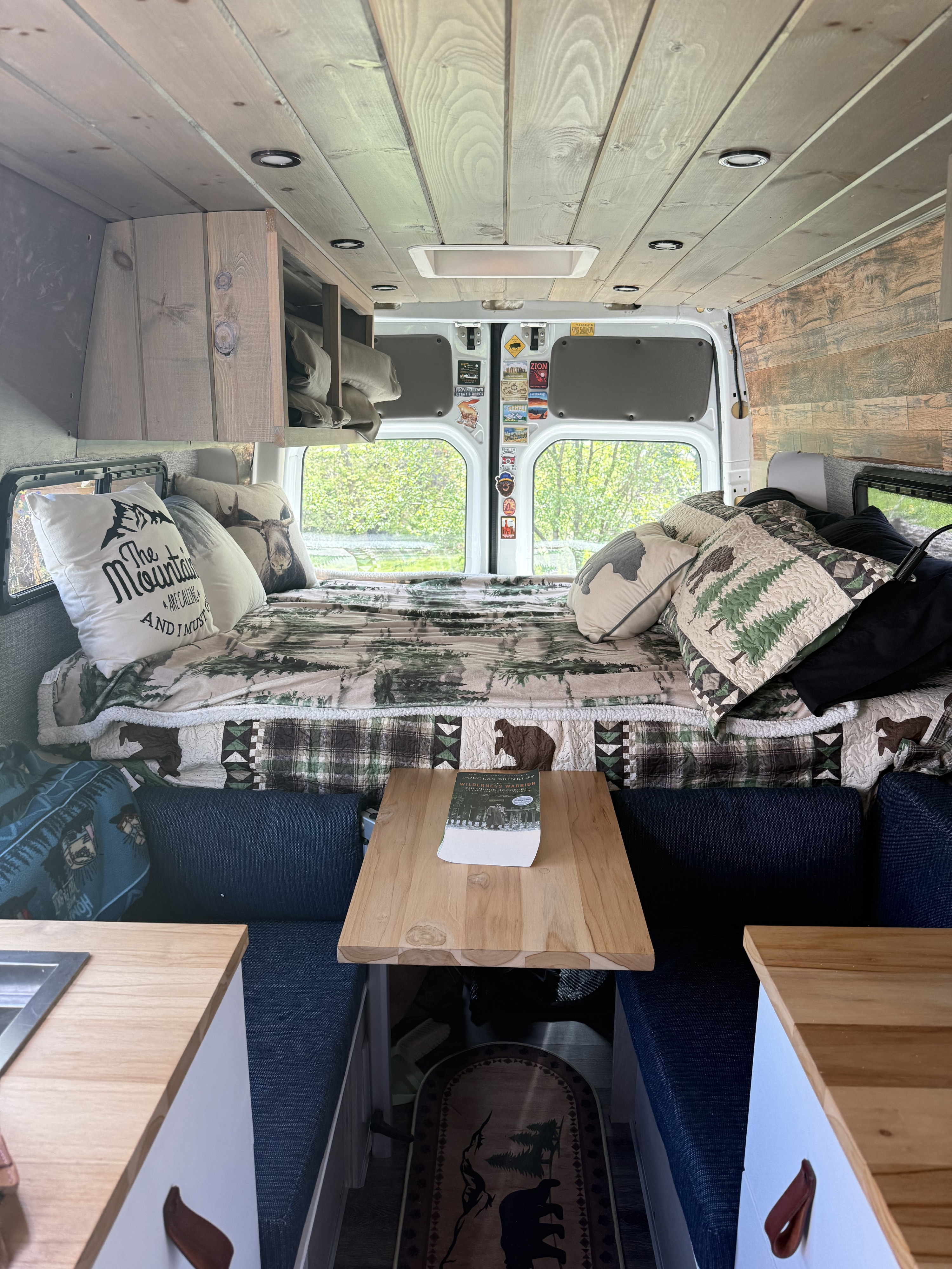 Cozy RV rental camper van interior: nature-themed bed, wooden ceiling/walls, kitchen, and dining nook for comfortable travel.. Mercedes Sprinter 2011