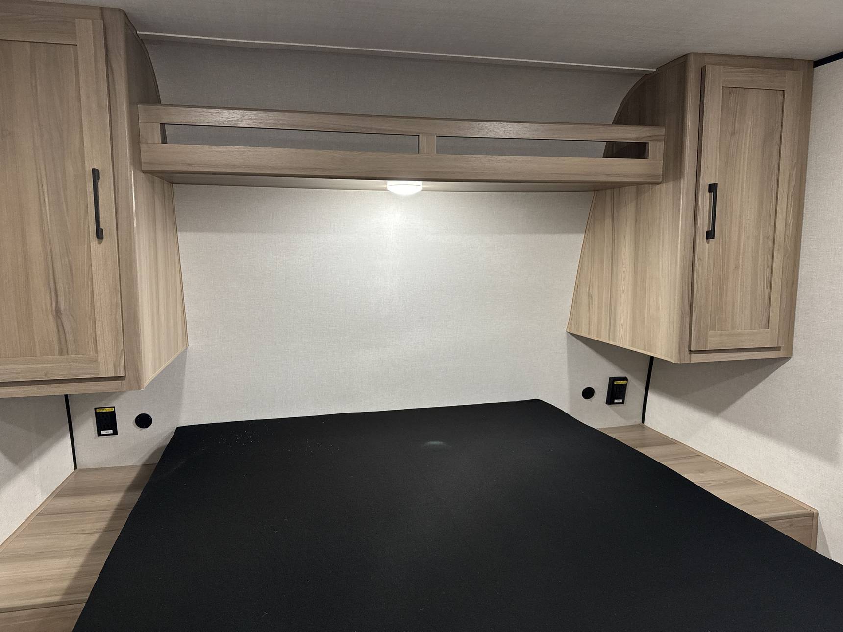 RV rental's cozy bedroom. Features a bed, light wood overhead cabinets, and convenient side charging ports. Bright & functional space.. Keystone RV Coleman Light 2025