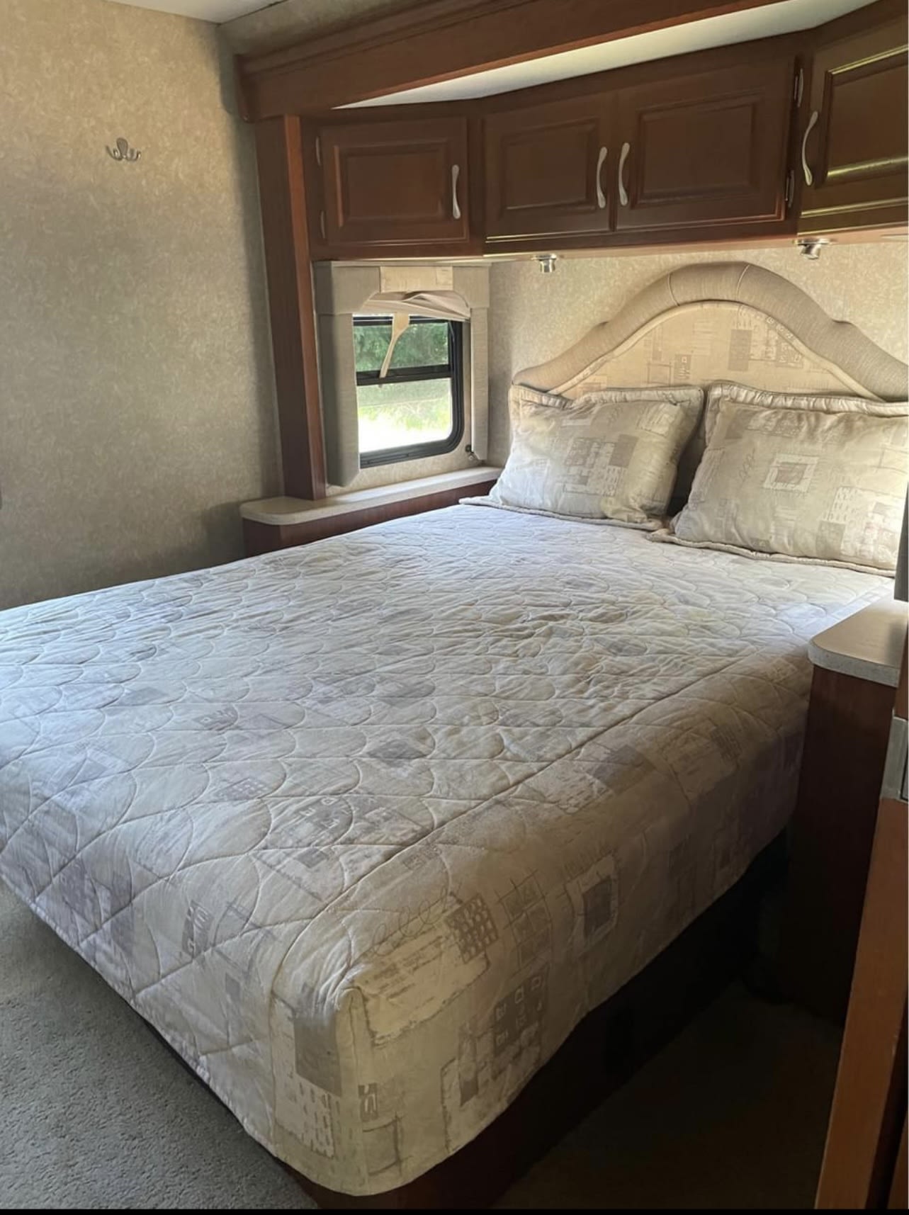 RV rental bedroom: quilted bed, upholstered headboard, overhead cabinets, and a window for comfortable travel.. Four Winds Hurricane 2007