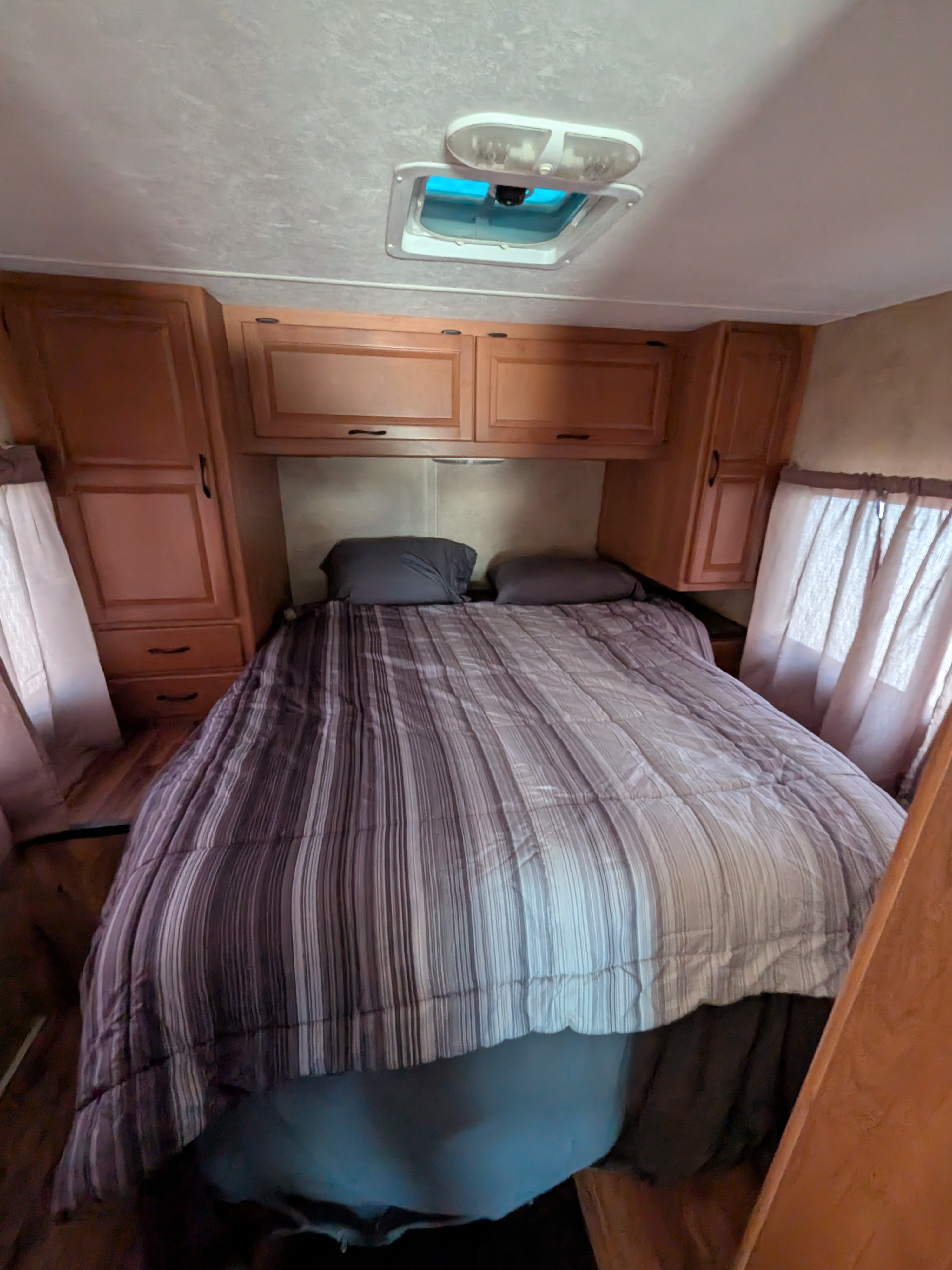 Cozy RV rental bedroom with striped bed, wooden cabinets, and ceiling vent, offering comfort for your travels.. Thor Majestic 2014