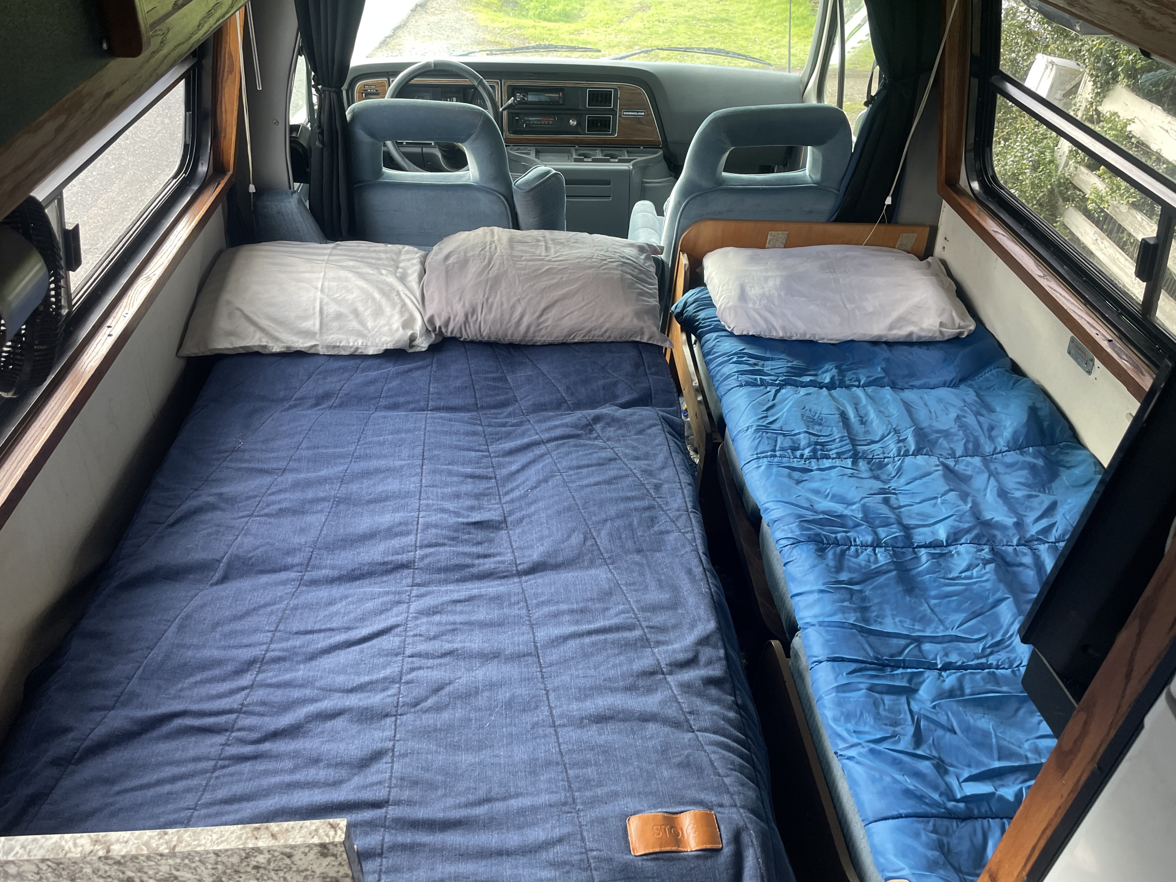 Cozy rv rental interior: two blue beds, pillows, and a view into the driver's cabin and windows. Perfect for travel!. Ford Coachman 1990