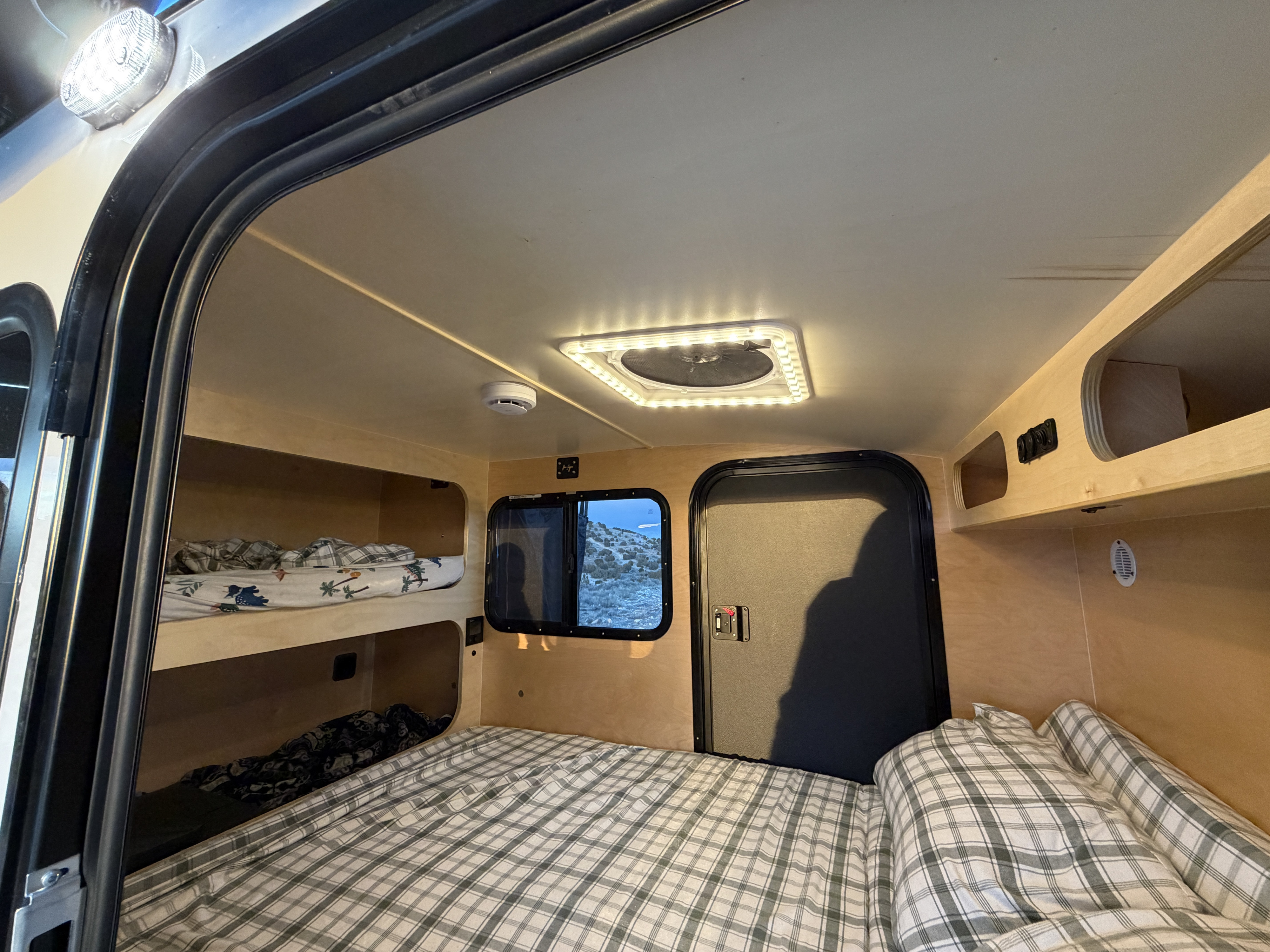 RV rental interior features cozy bunk beds, plaid main bed, scenic window view, and light wood finish. Perfect for travel!. Hike Mid range 2025