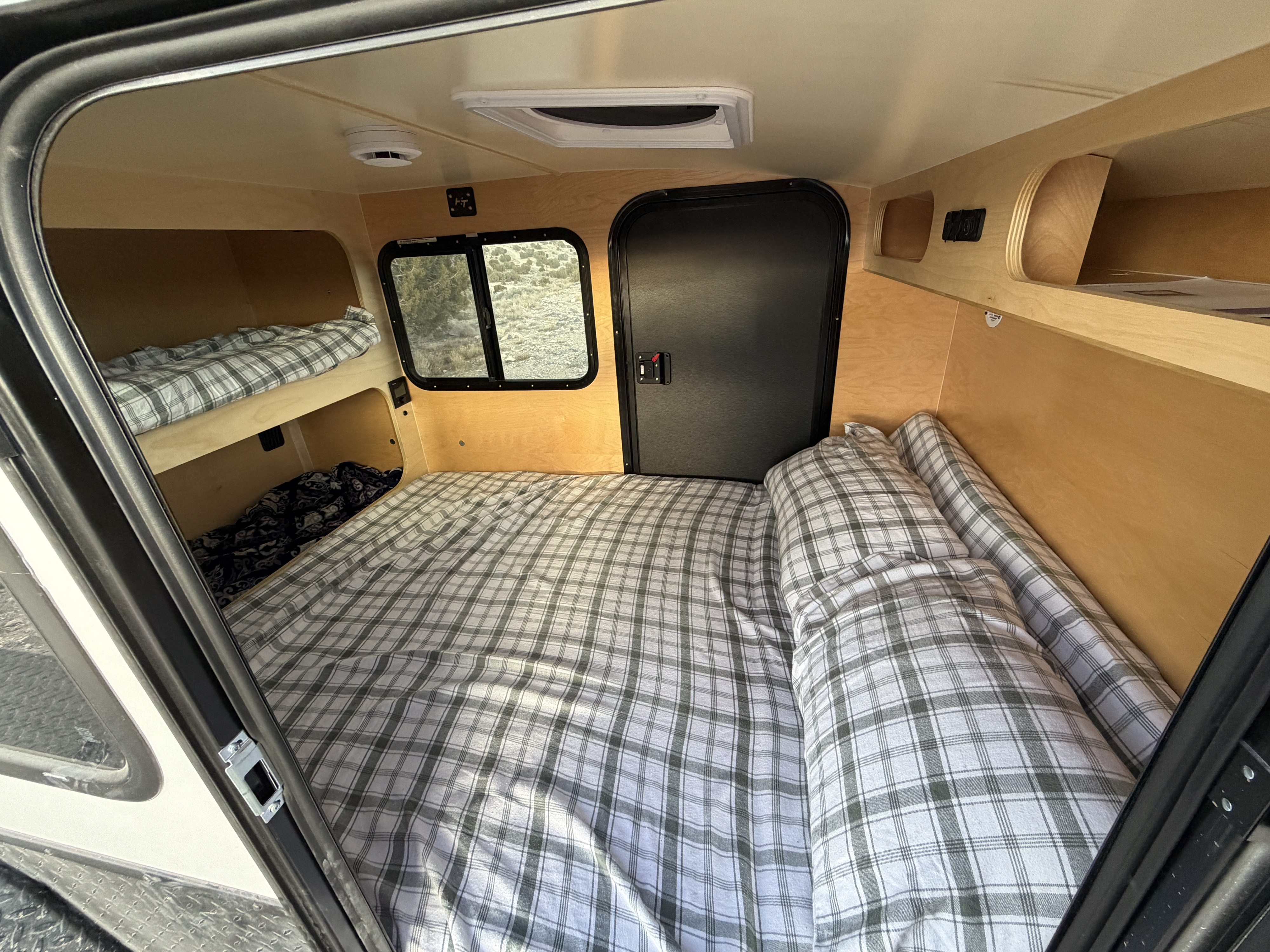 Cozy RV rental interior: main bed, bunk beds with plaid bedding, window, and storage. Perfect for camper travel.. Hike Mid range 2025
