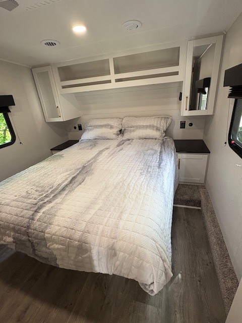 Experience comfort in this RV rental bedroom: queen bed with grey bedding, white cabinets, dark nightstands, and hardwood floors.. Jayco Eagle 2026