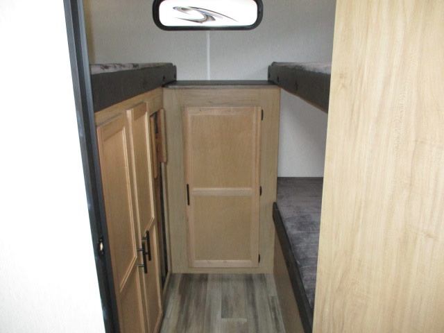 Compact rv rental interior with stacked bunk beds and wooden storage cabinets on each side, along a central aisle.. Forest River Cherokee Grey Wolf 2023